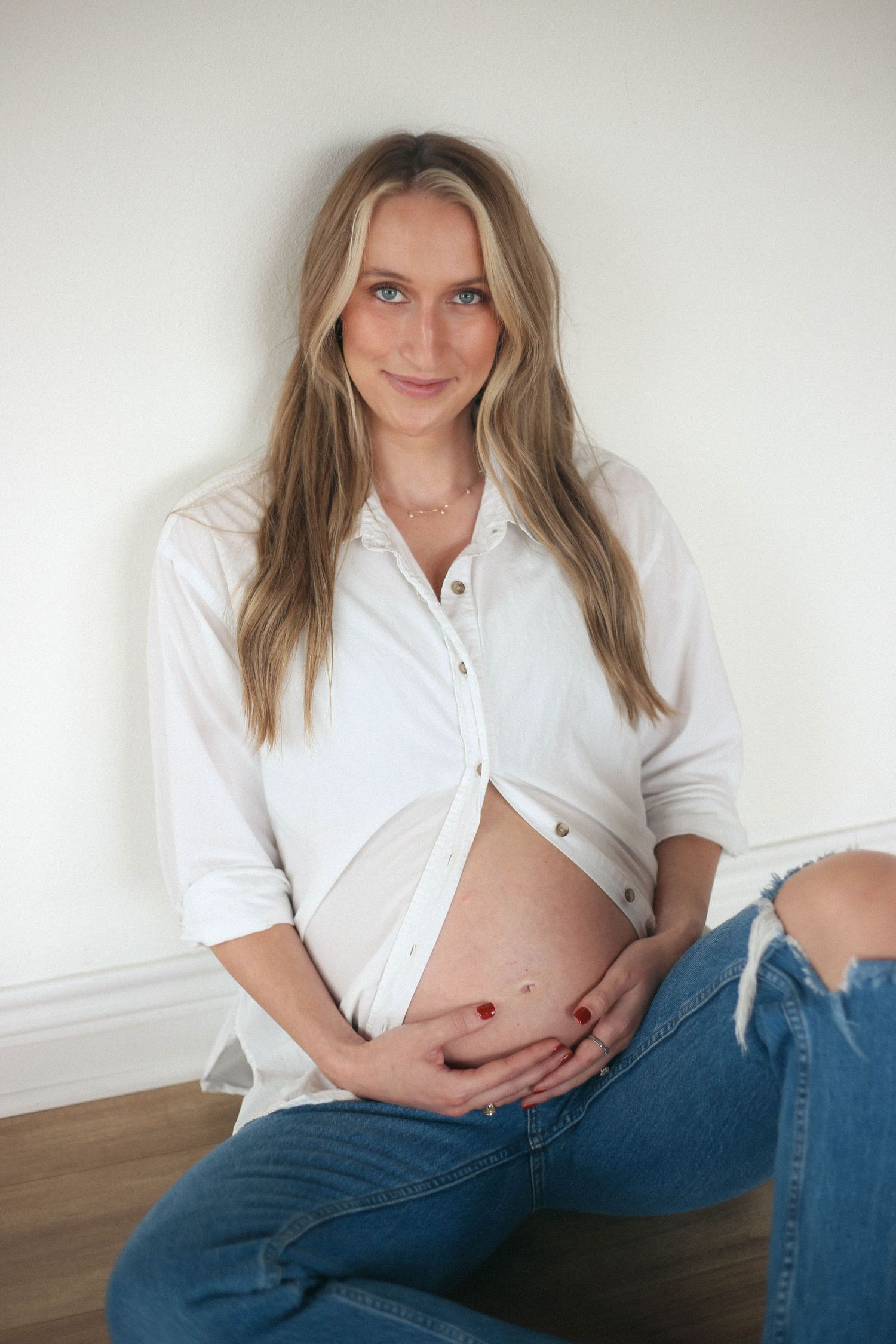 A maternity portrait featuring a woman in a white button-down shirt revealing her baby bump.