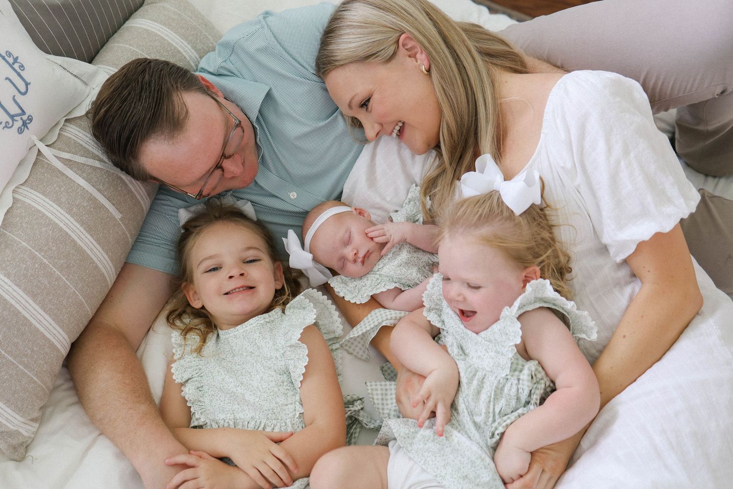 Happy family of five with parents and three young children, including a newborn, relaxing together on a cozy bed.