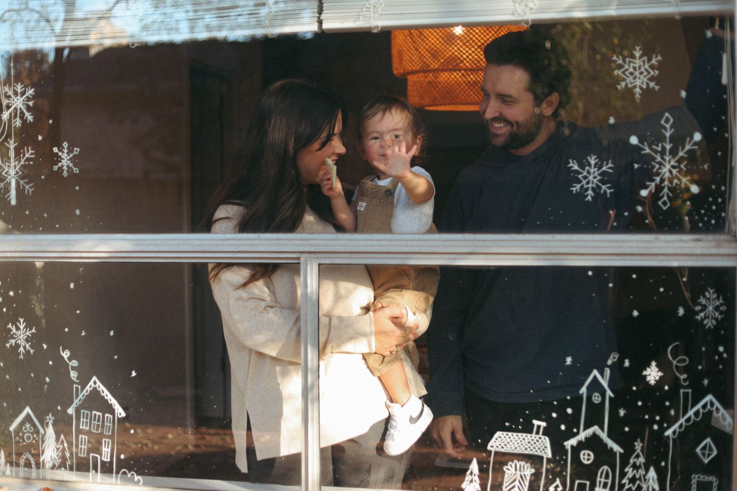 Family looking through window decorated with winter holiday designs.