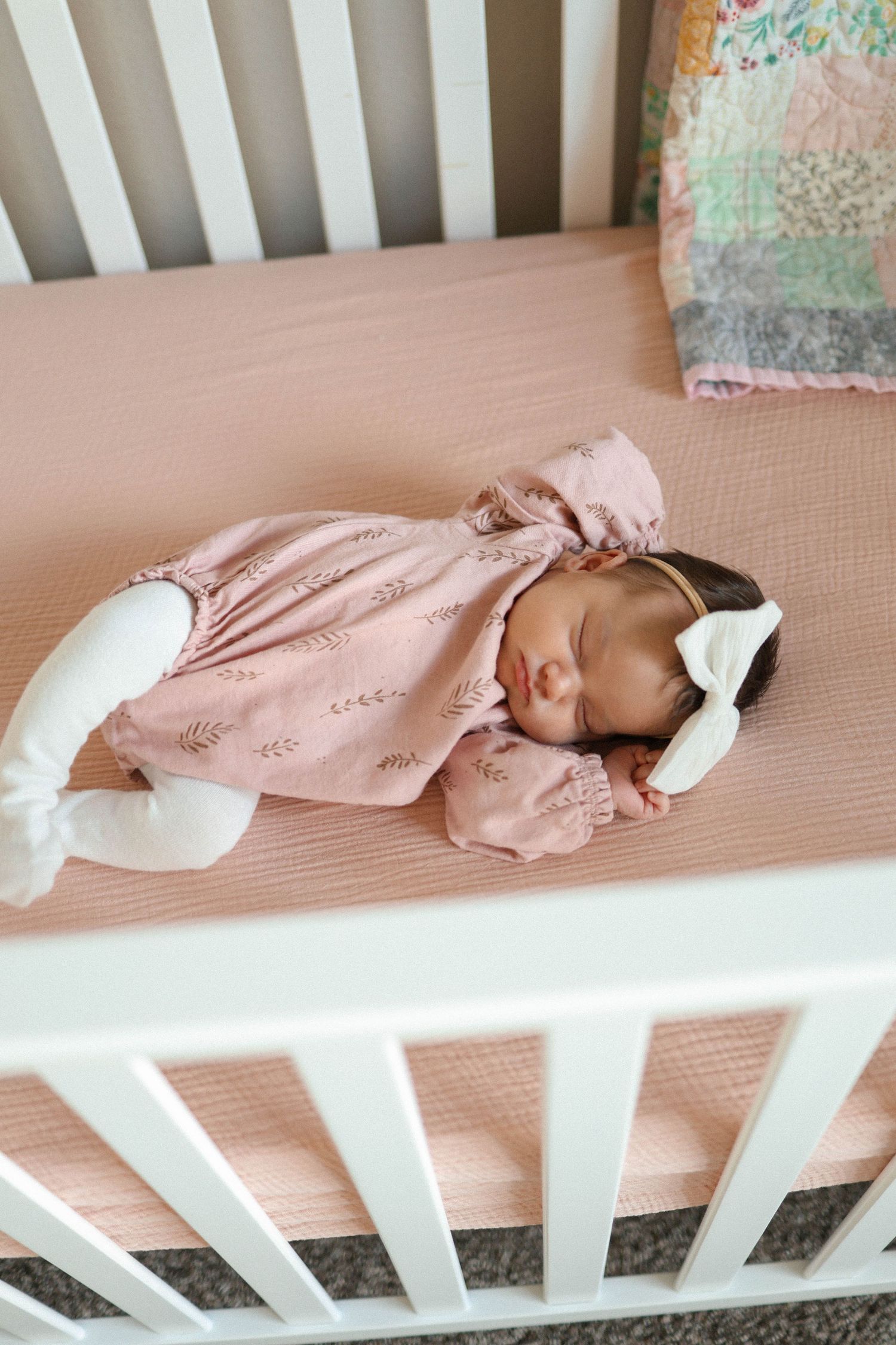 Baby sleeping peacefully in pink outfit on pink crib mattress.