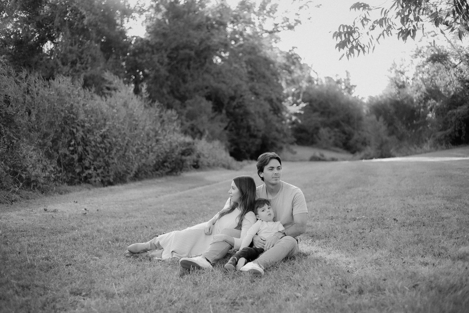 A couple and their young boy sit together on grass in a dreamy black and white photo.