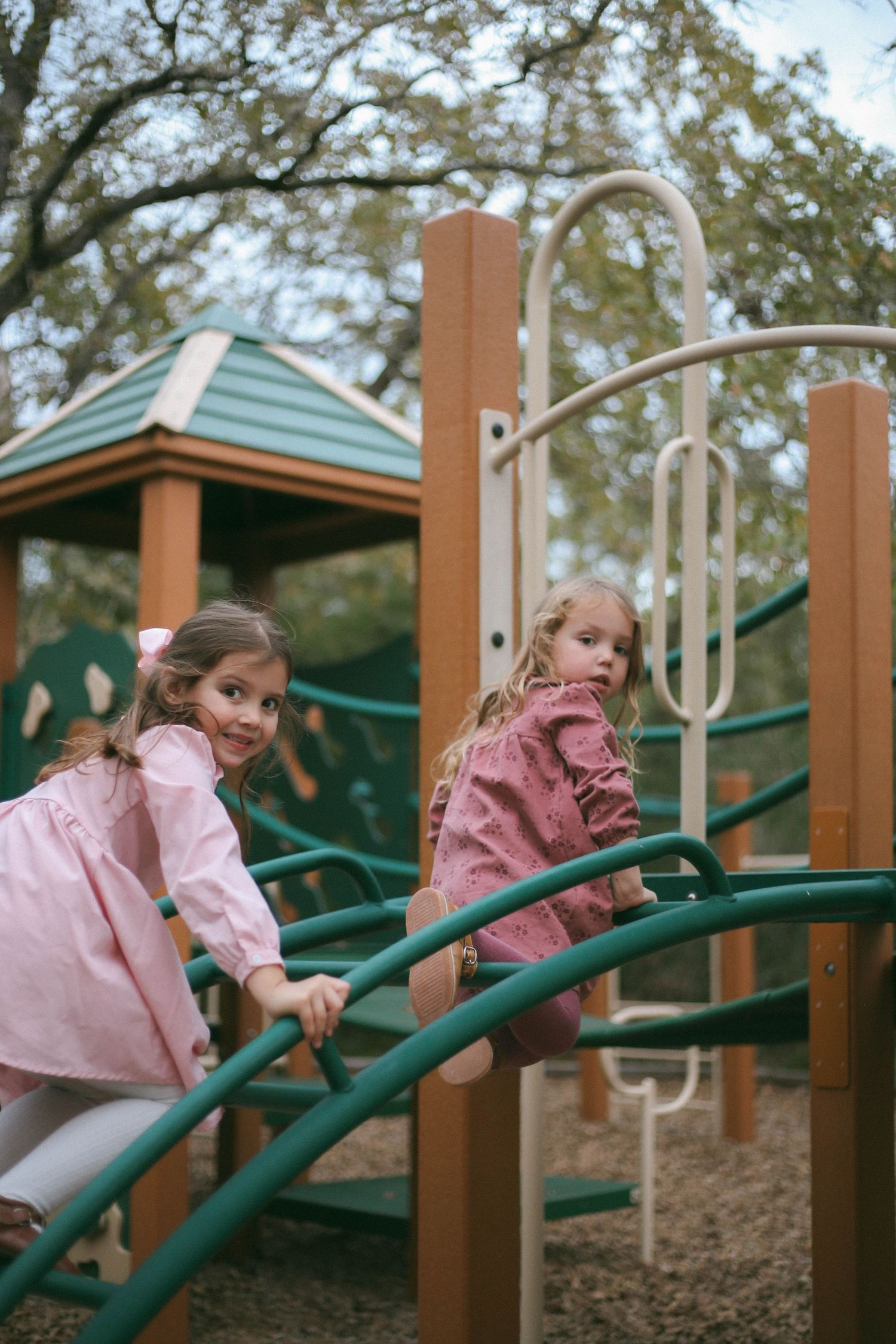 Young child in pink jacket climbs on playground equipment during outdoor play sequence.