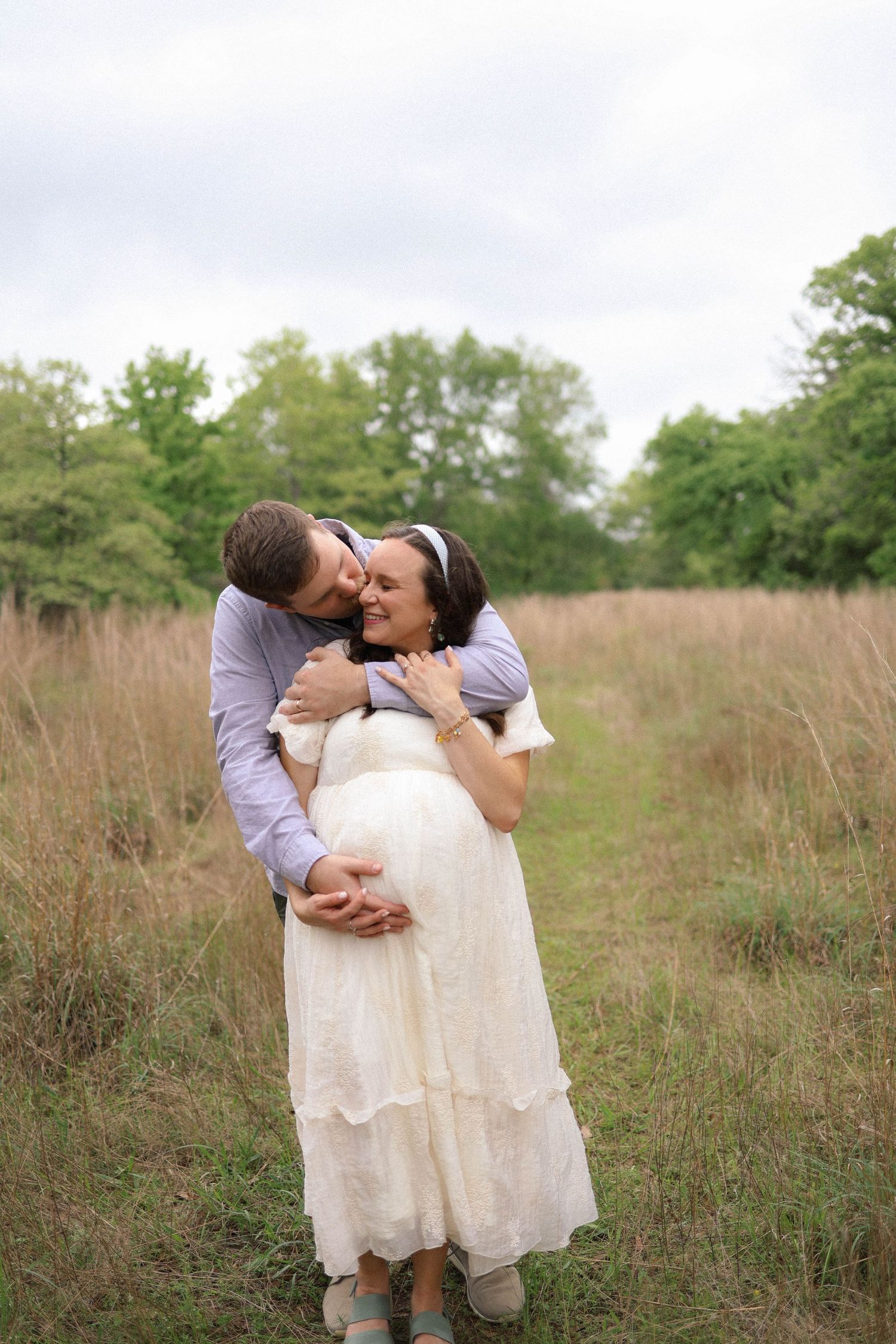 A romantic maternity photo of a couple embracing in a sunlit meadow with tall grass.