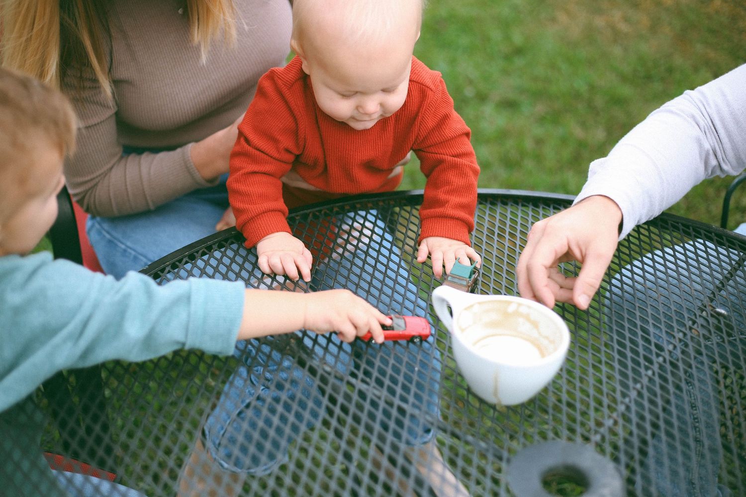 Close-up series of small hands playing with toy cars on outdoor table at a coffee shop with family.
