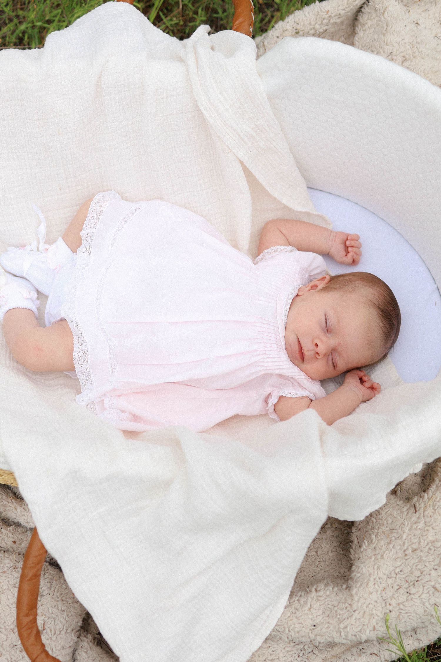 Newborn baby sleeping peacefully in a wicker Moses basket lined with soft white blankets, wearing a pink outfit.
