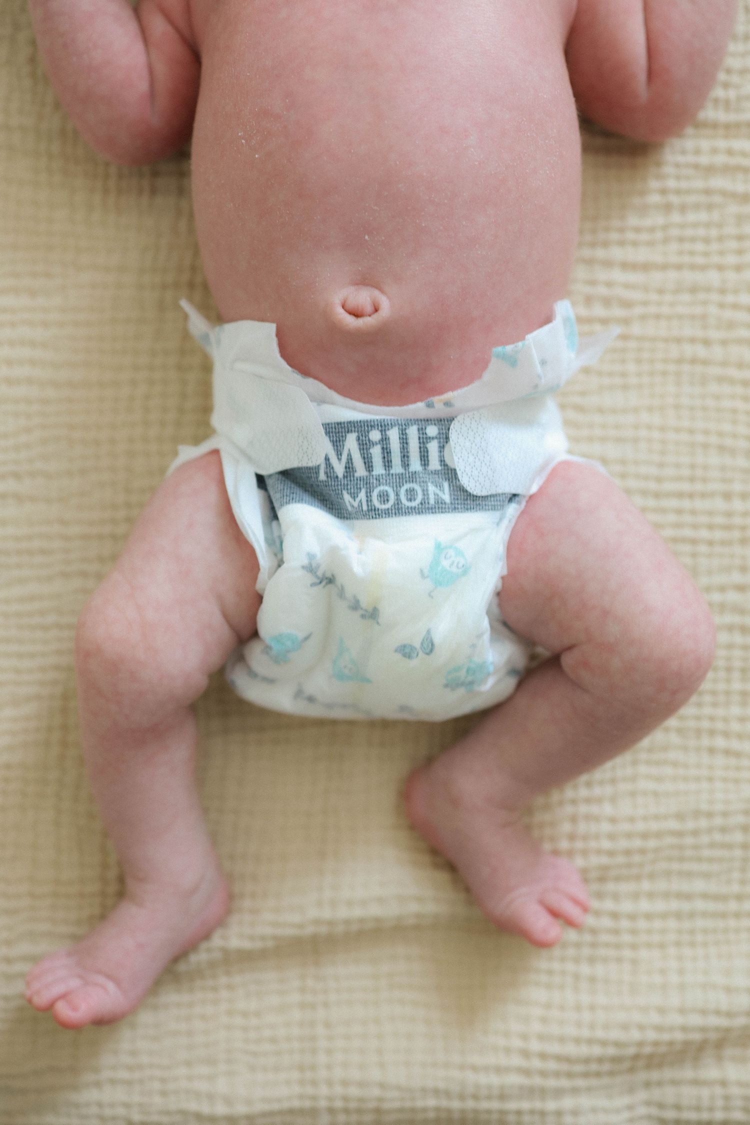 Close-up of a newborn baby wearing a Millie Moon diaper, lying on a yellow blanket.