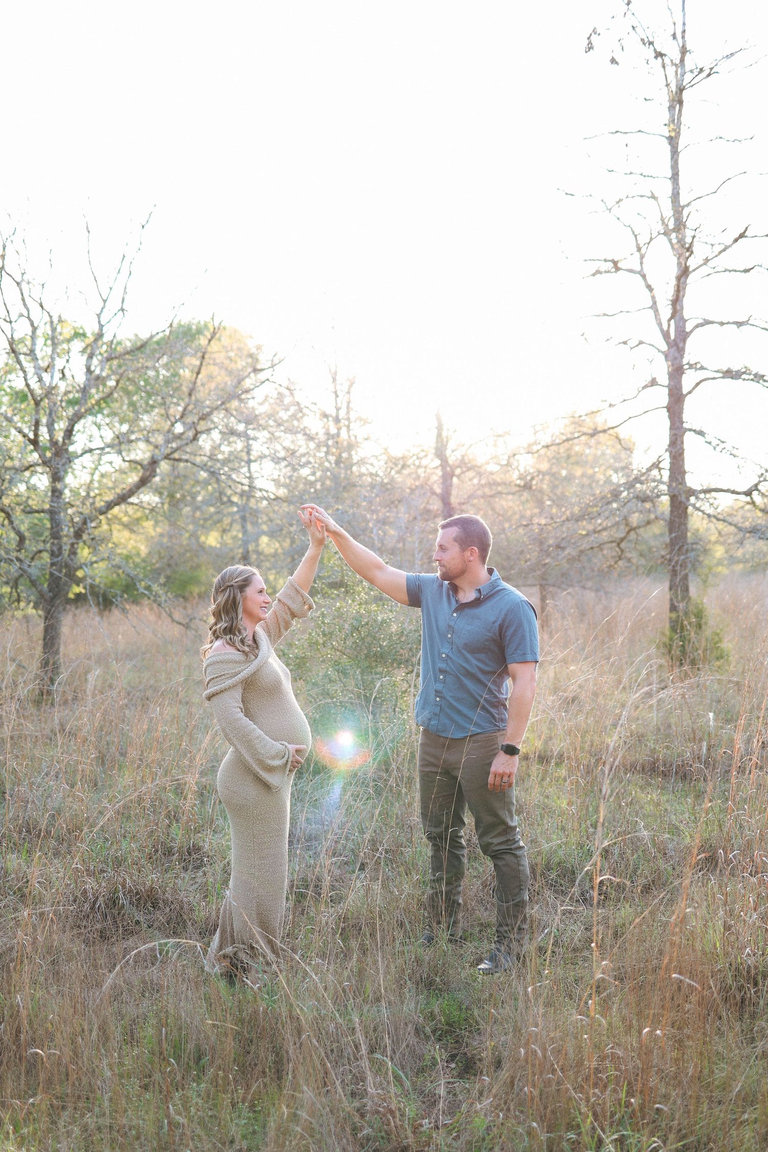 A couple celebrating in a field during golden hour with playful poses and expressions during maternity session.