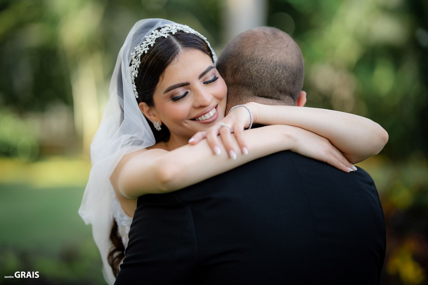 A bride in a white wedding gown embraces her partner during an outdoor garden ceremony.