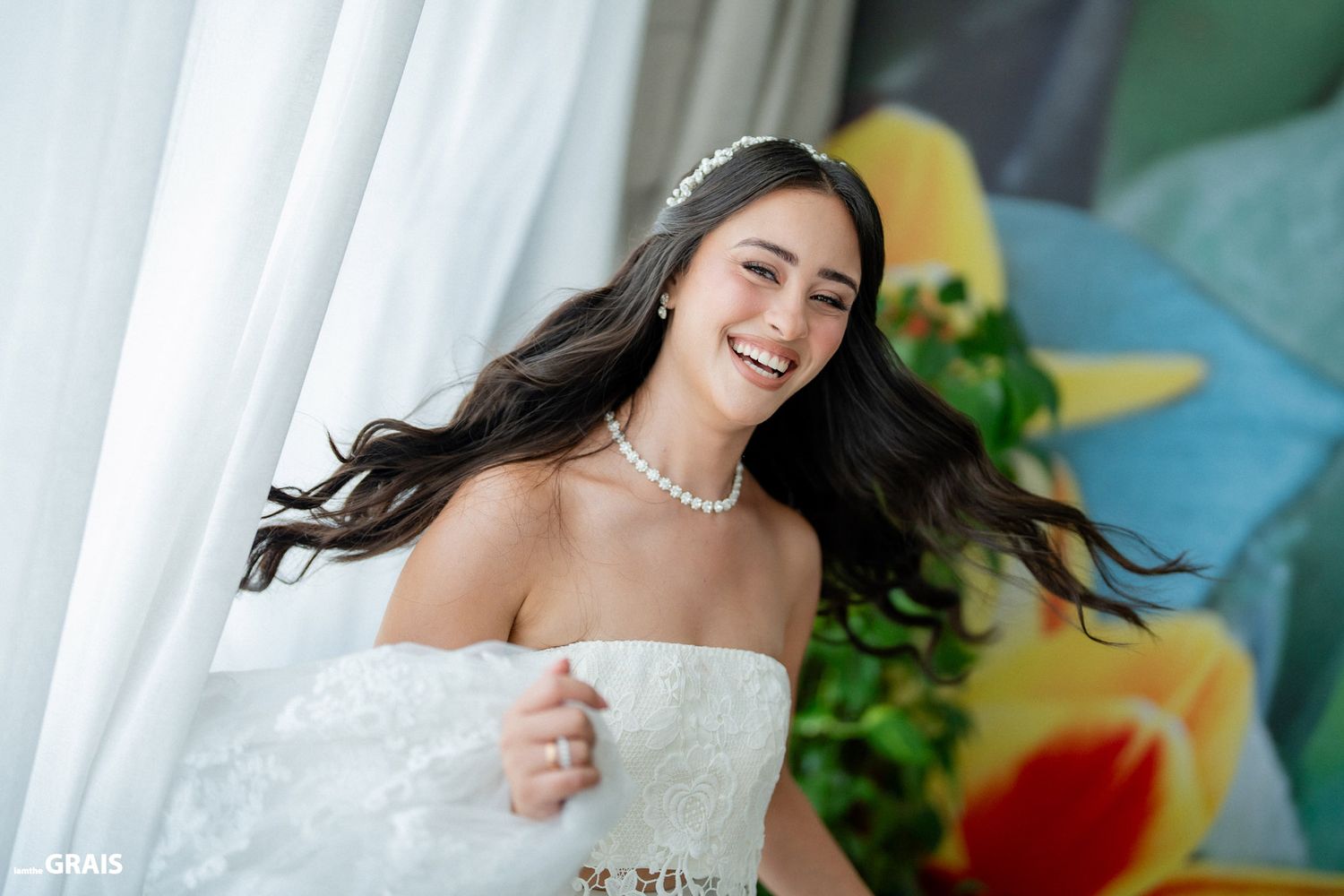 A joyful bride in a strapless wedding dress twirls with flowing hair against a bright backdrop.