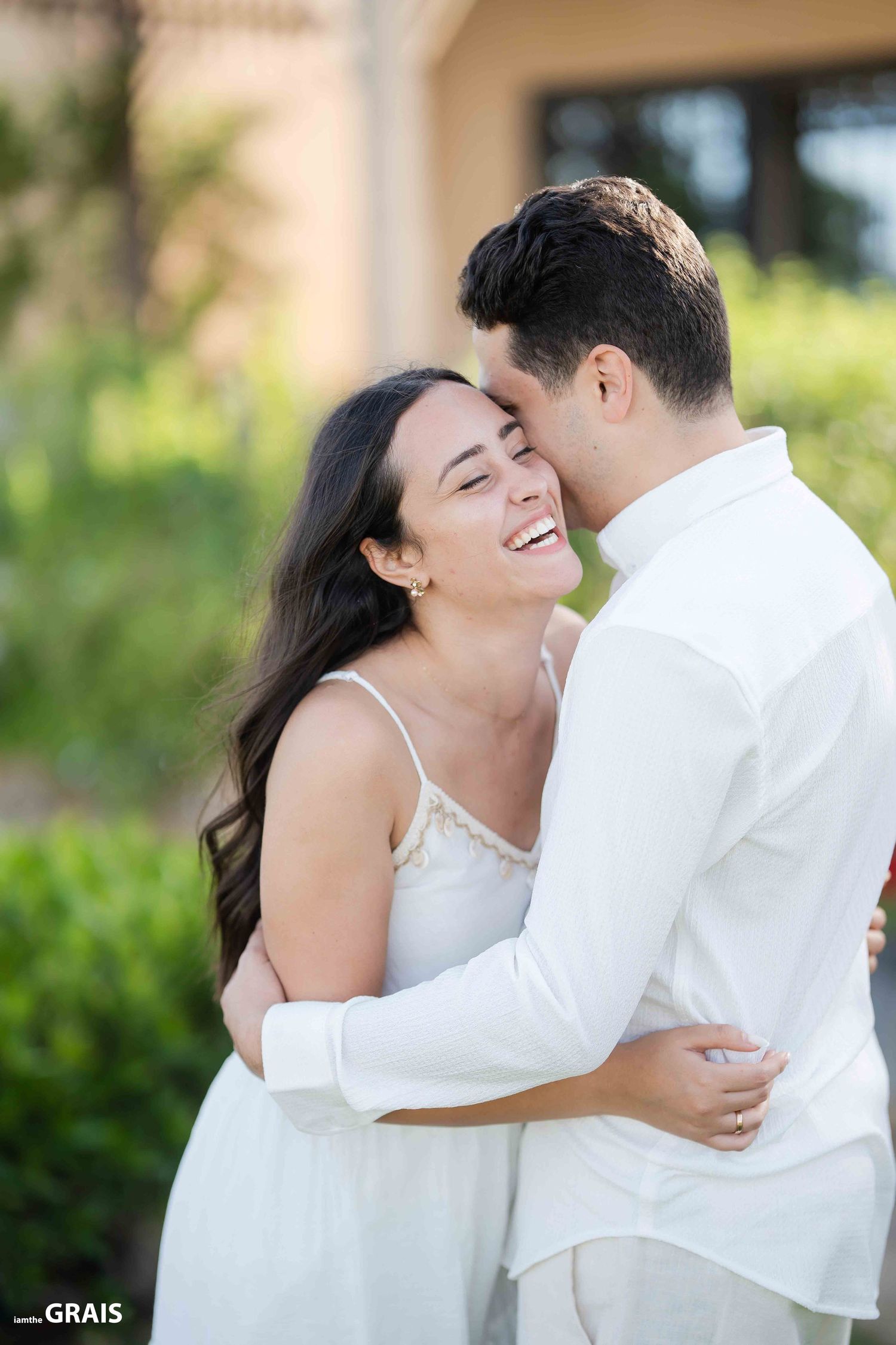 Romantic couple sharing intimate moment in garden setting wearing white attire.