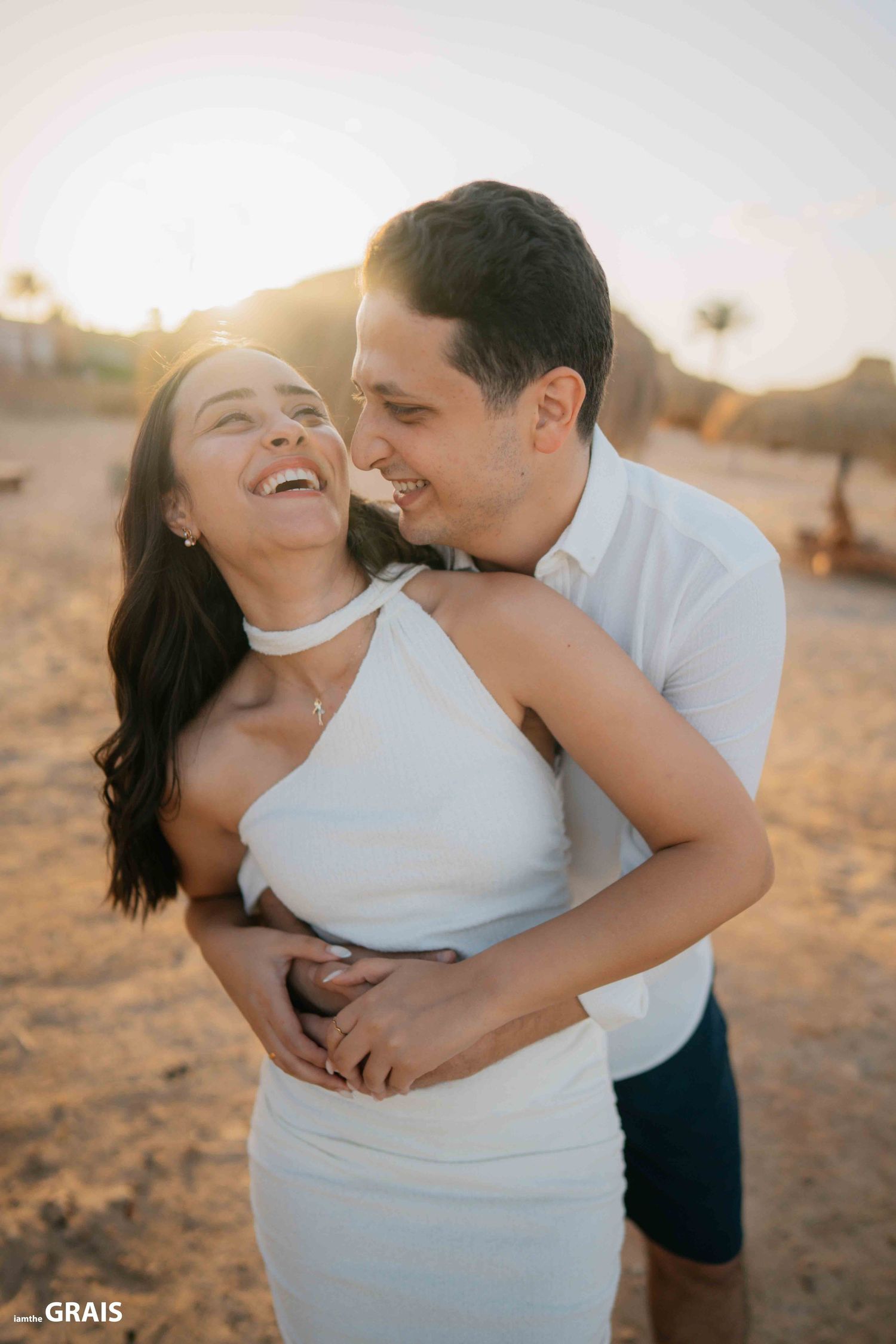A couple laughs together during a sunset photoshoot on the beach.