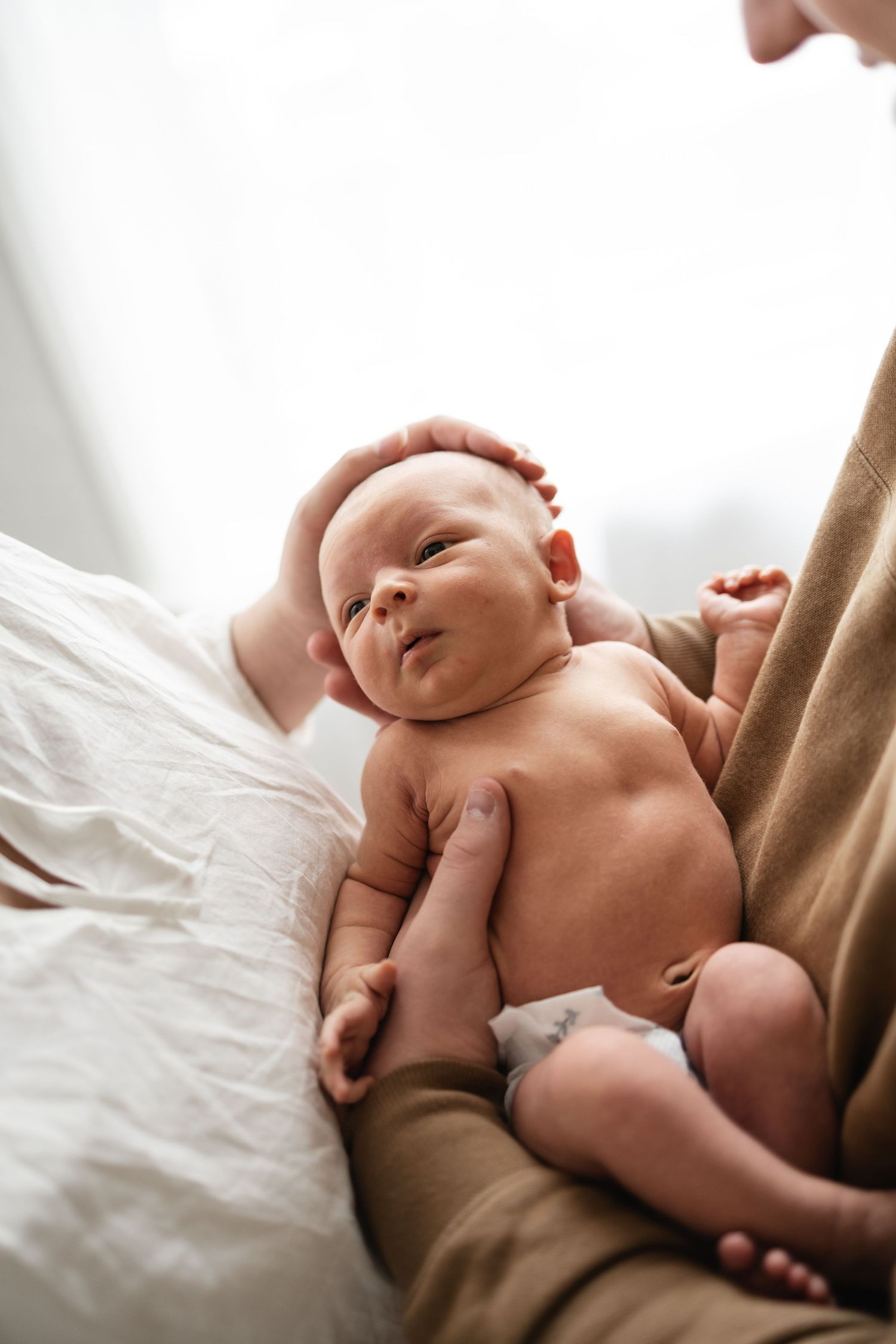 Newborn baby lying on white bedding with parent's arm visible in tender nurturing moment taken by Woodbury newborn photographer.