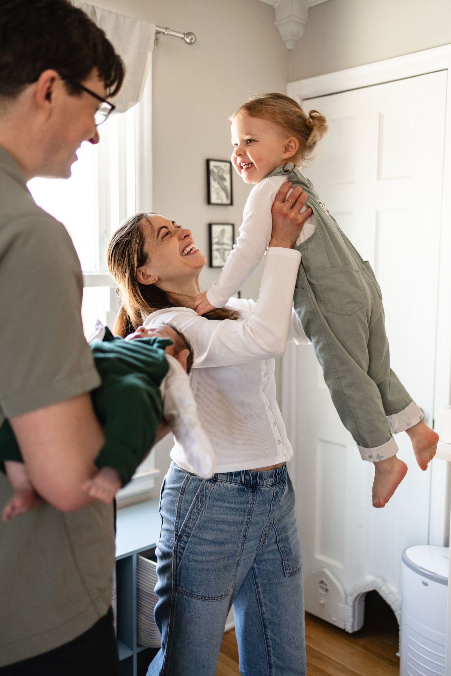 A sequence of photos showing a couple dancing and laughing together with their newborn and toddler in a bright bedroom.