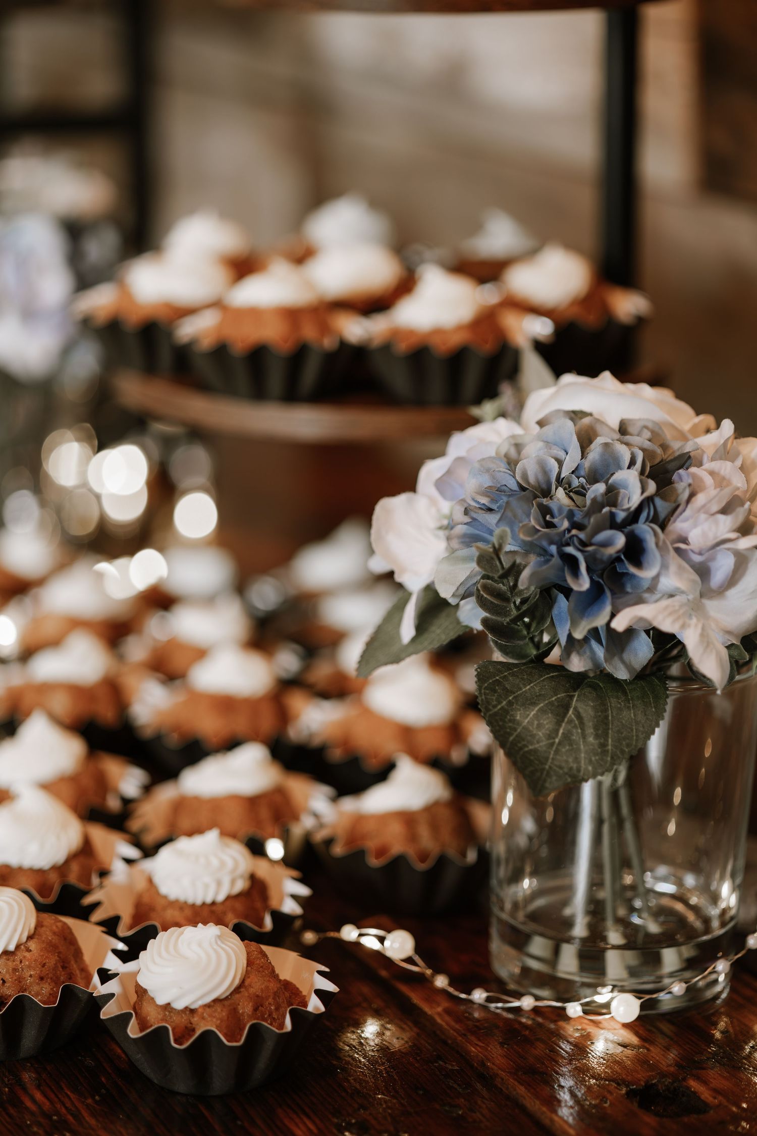 Mini tarts with white cream frosting displayed on a rustic wooden table beside a vase of blue and white hydrangeas.