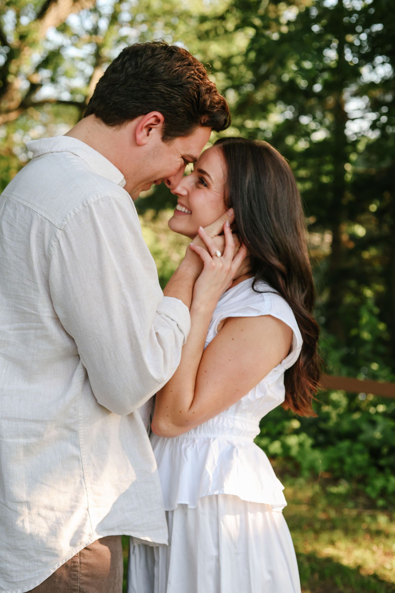 Engagement captured by Woodbury photographer shows couple in white clothing share tender kisses while embracing in a sunlit garden setting.