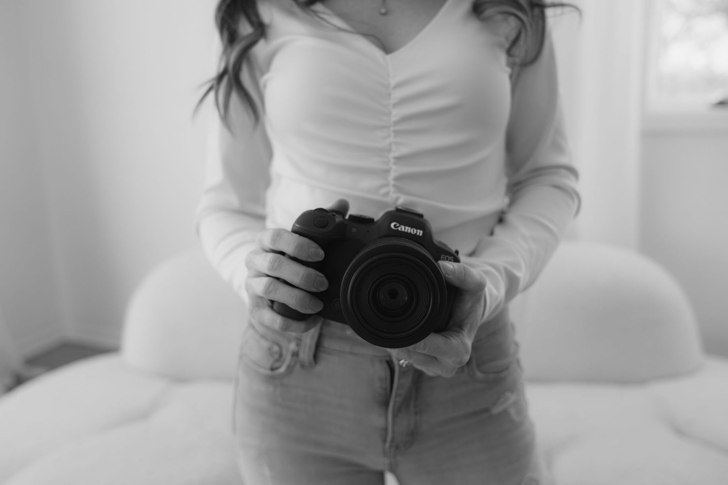 A Twin Cities photographer in white top holding a professional camera while standing against a light background.