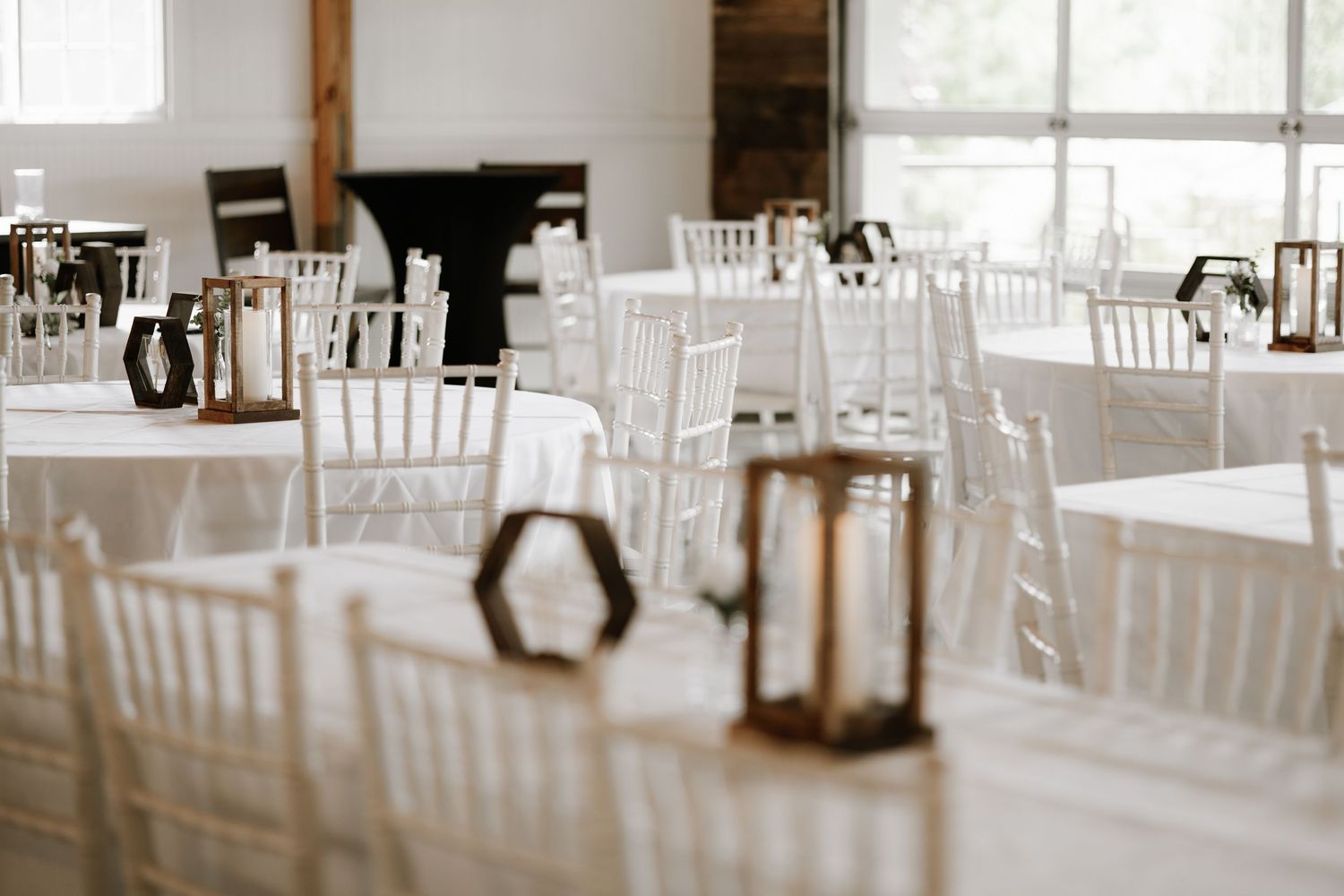 Elegant wedding reception hall with white Chiavari chairs, round tables with white linens, and rustic lantern centerpieces.