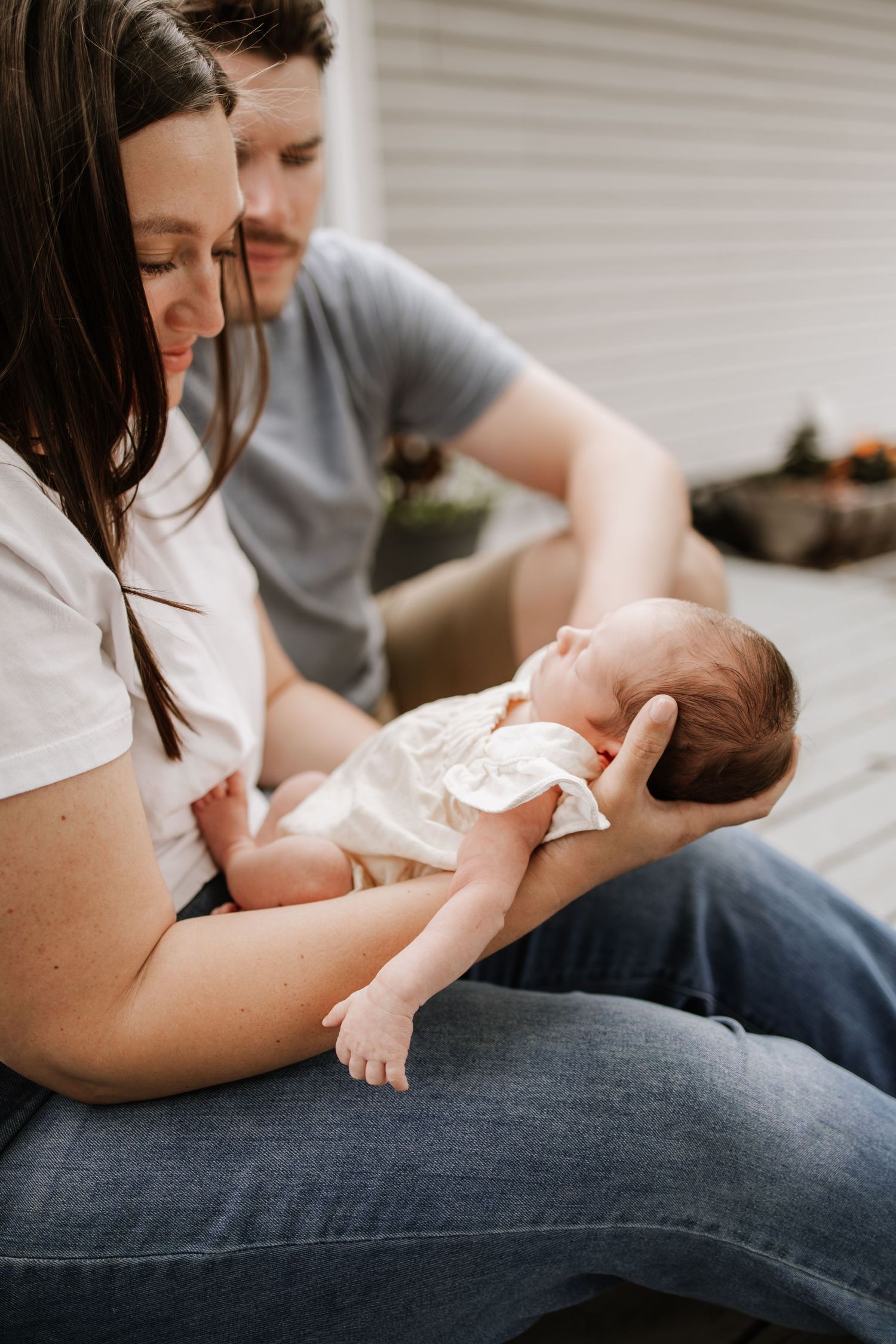 New parents sitting outdoors lovingly cradling their sleeping newborn baby during a tender in home newborn session in Minneapolis.