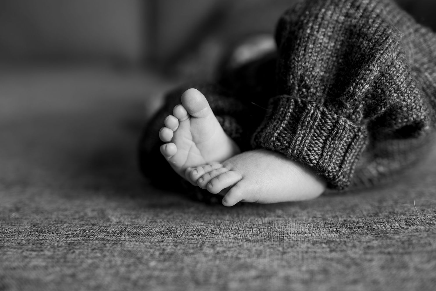 Black and white close-up of newborn baby's tiny feet wrapped in a cozy knit blanket during in-home session by Woodbury newborn photographer