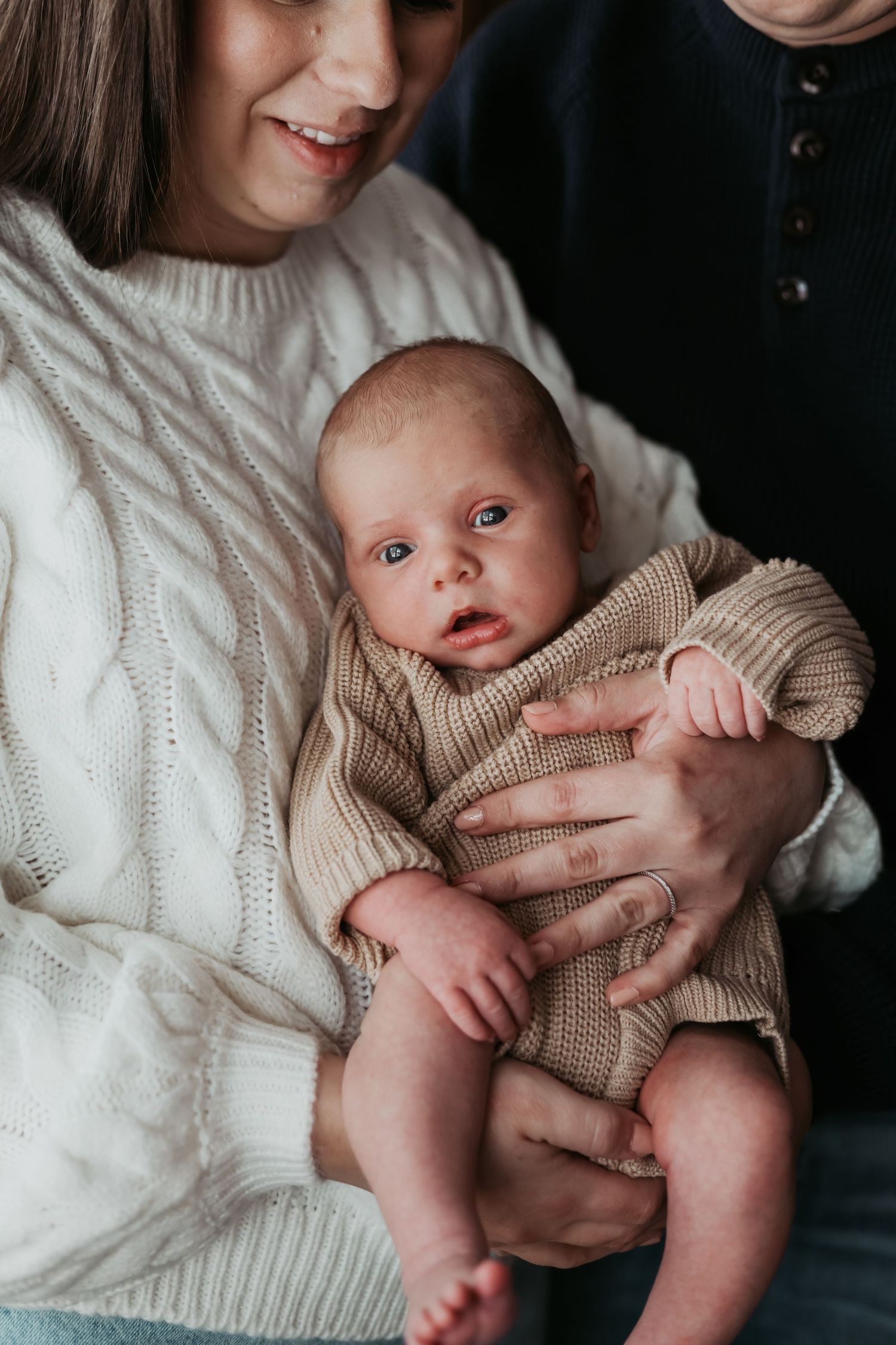A tender moment showing a baby in a beige sweater being cradled against white knitwear captured by Woodbury newborn photographer.