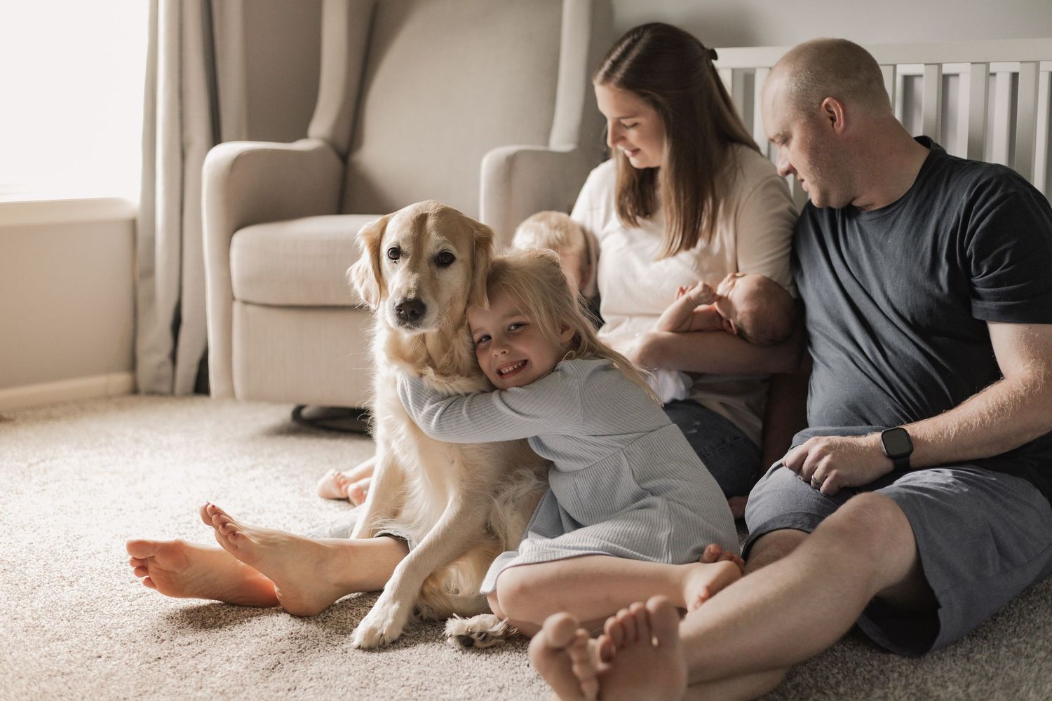 A family sits together on the floor with their golden retriever dog in a cozy living room setting during Lakeville in-home newborn session.