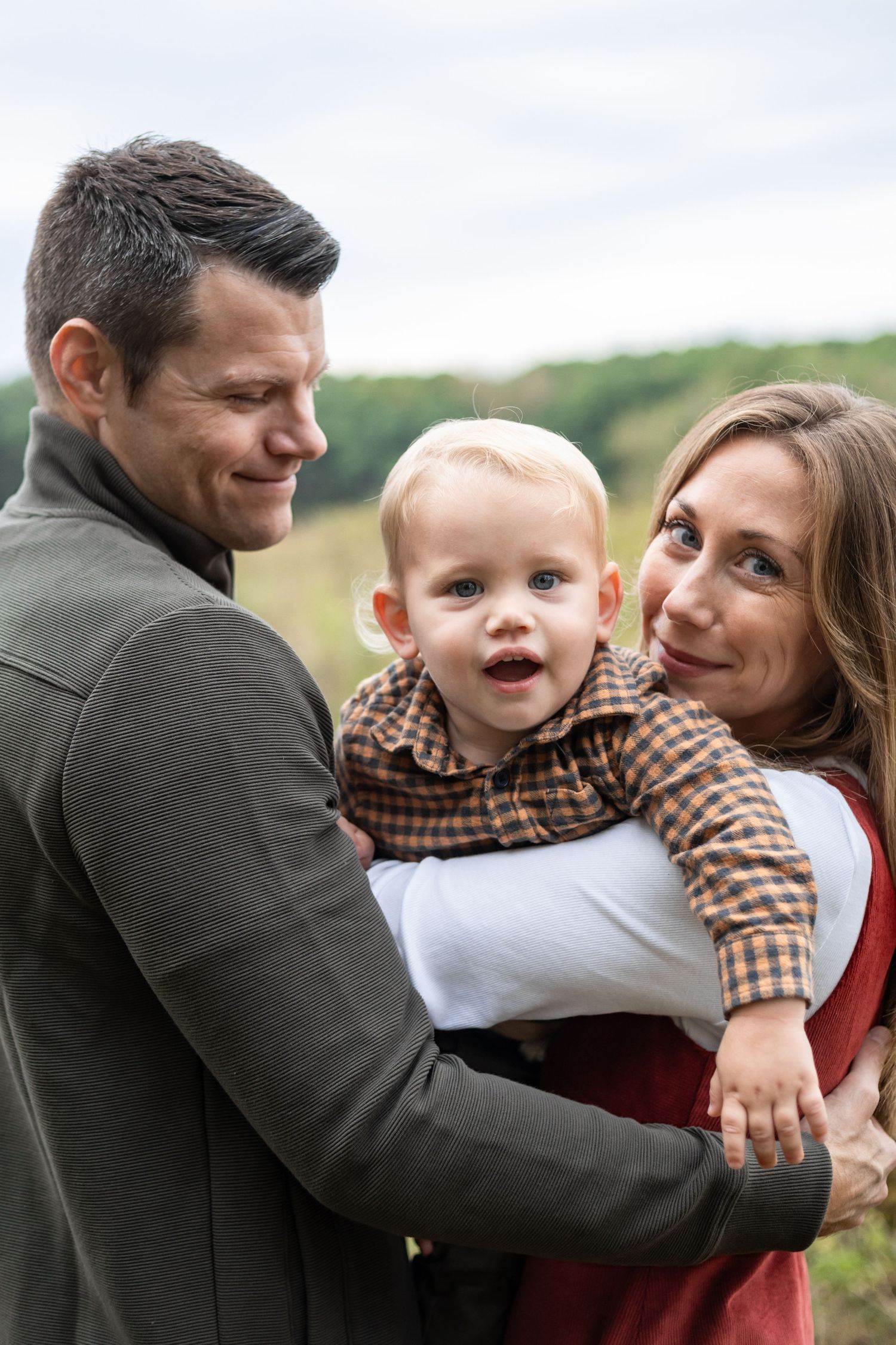 A happy family with a toddler boy outdoors during a fall family mini session taken by Kelly Christine Photography.
