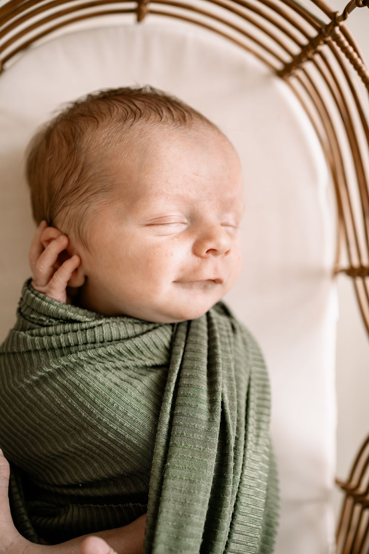 Peacefully sleeping newborn baby swaddled in a green ribbed wrap, resting in a wicker bassinet in studio newborn session in Lakeville.