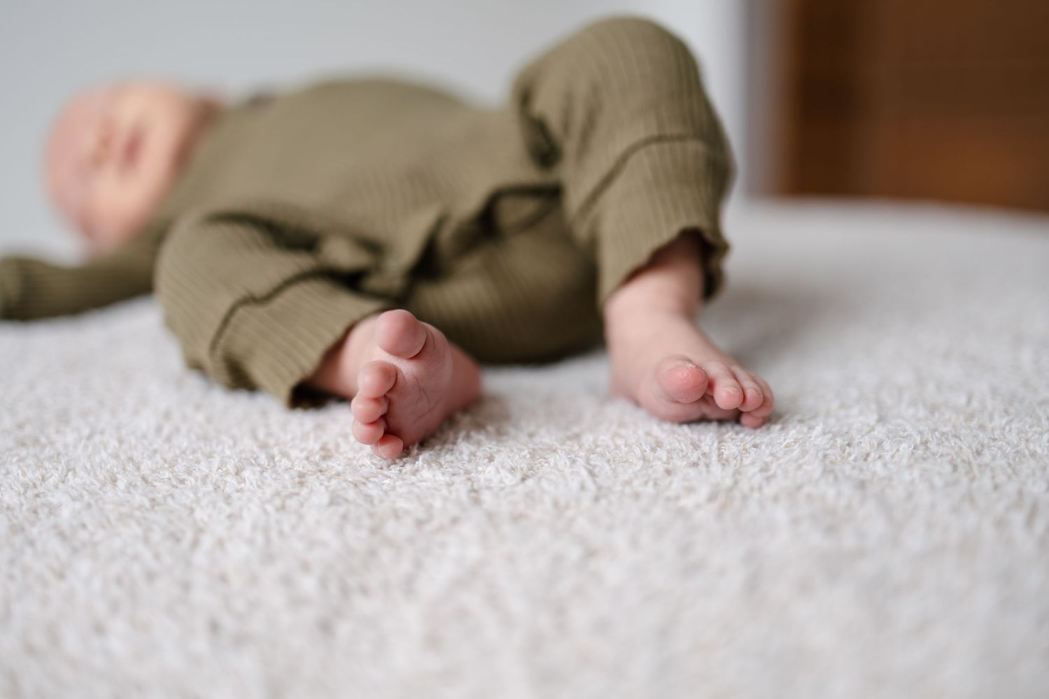 Tiny newborn baby feet with wrinkled skin resting on soft white textured fabric, taken by Woodbury newborn photographer.