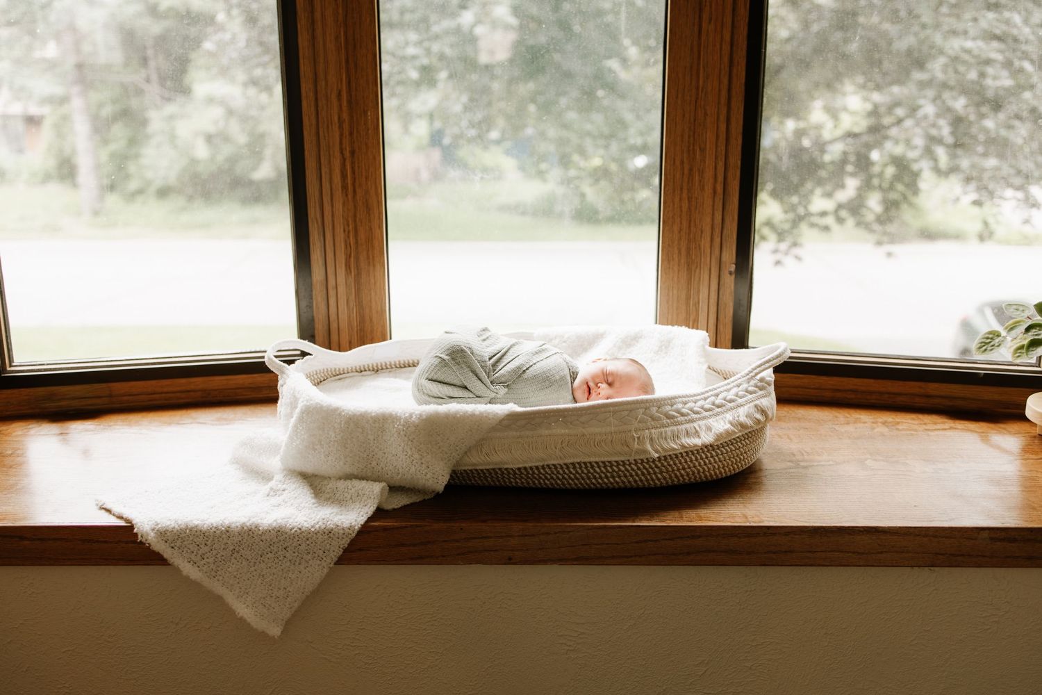Newborn baby sleeping peacefully in a basket on a wooden windowsill with soft natural light during lifestyle newborn photos in Minneapolis.