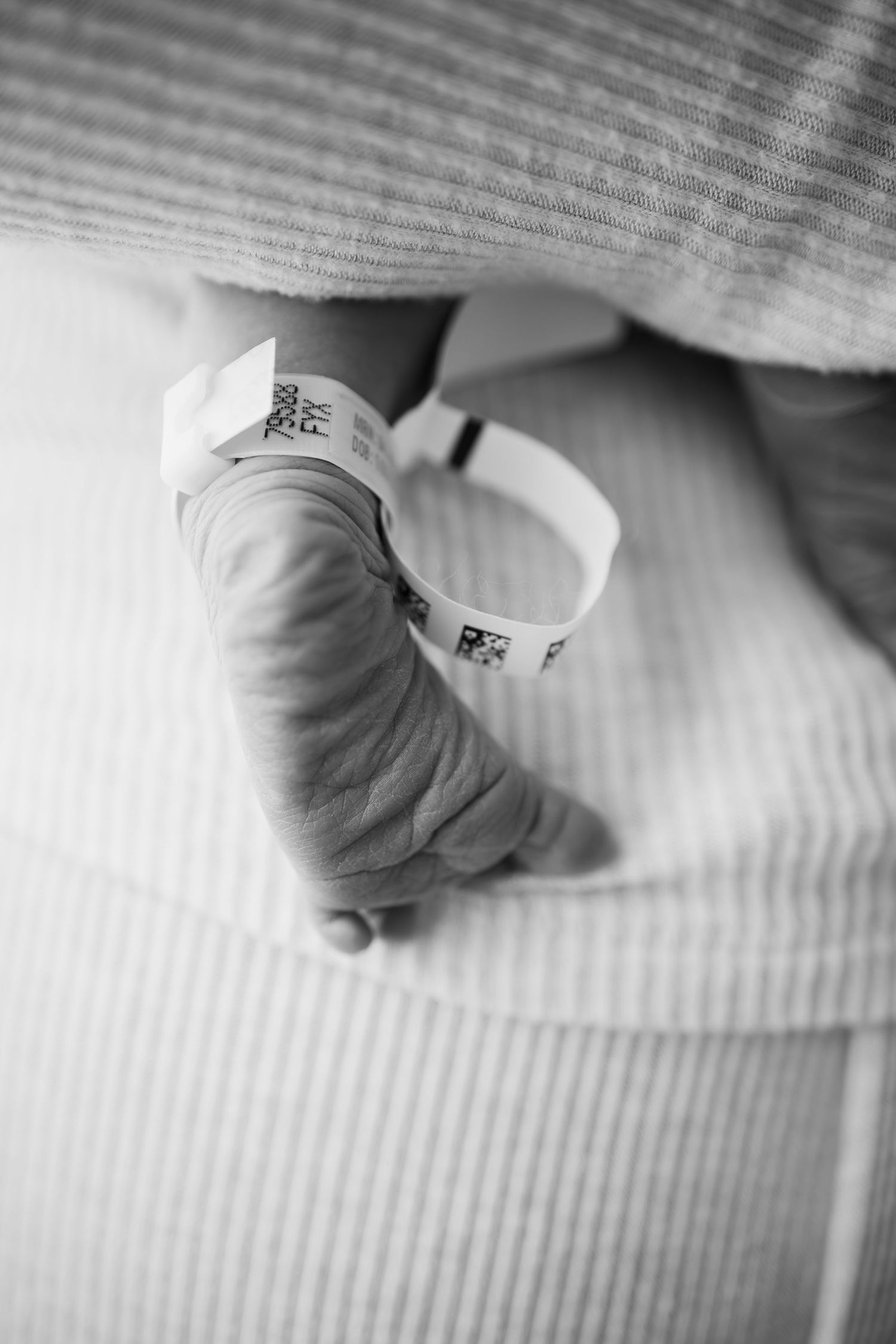 Black and white close-up photo showing tiny baby feet resting against a textured white surface taken by Woodbury newborn photographer.
