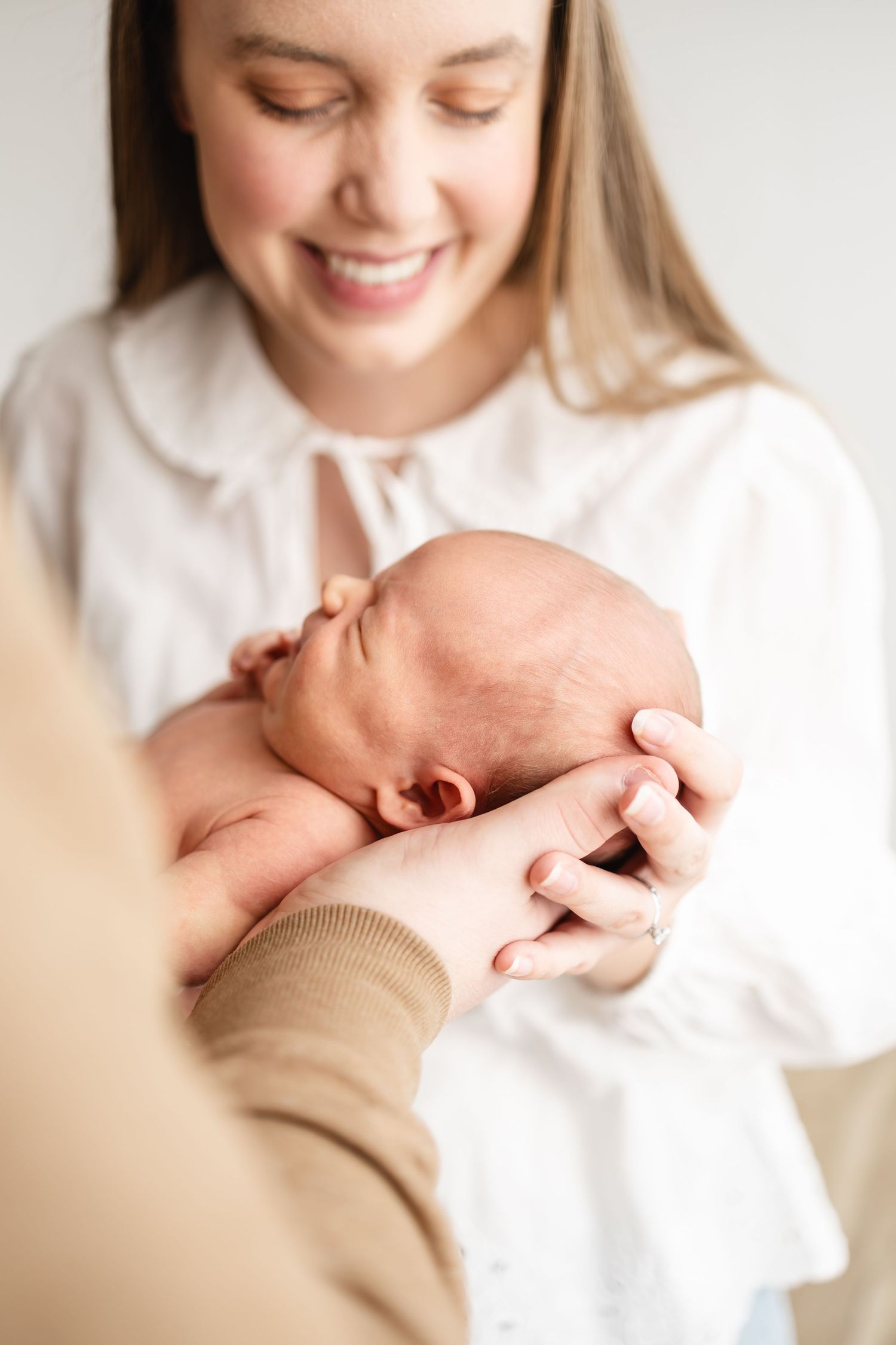 A tender moment as a newborn baby is gently cradled while being photographed by Woodbury newborn photographer in soft natural light.