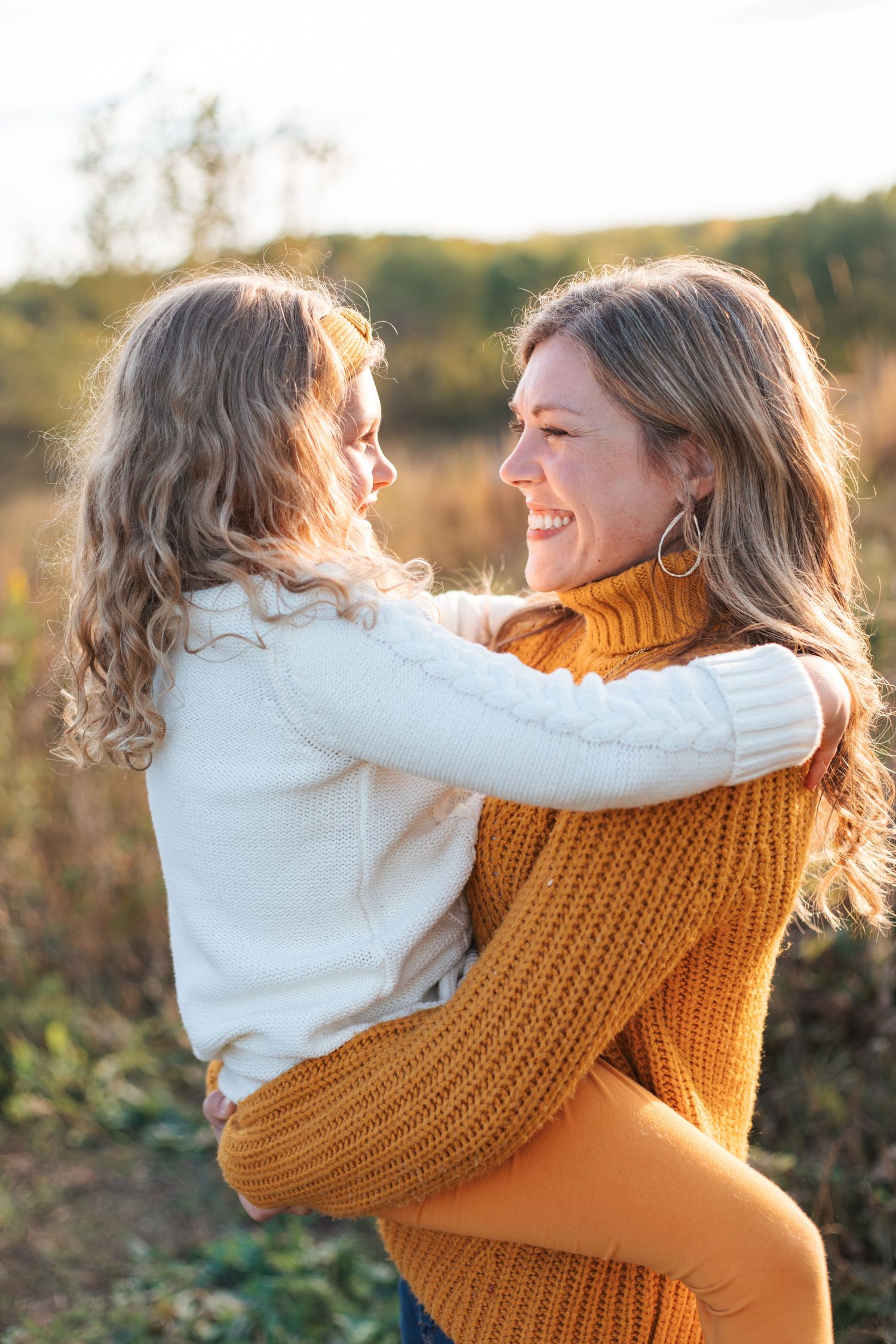 A heartwarming embrace between a mother and her child in autumn sunlight, wearing cozy sweaters taken by Lakeville family photographer.