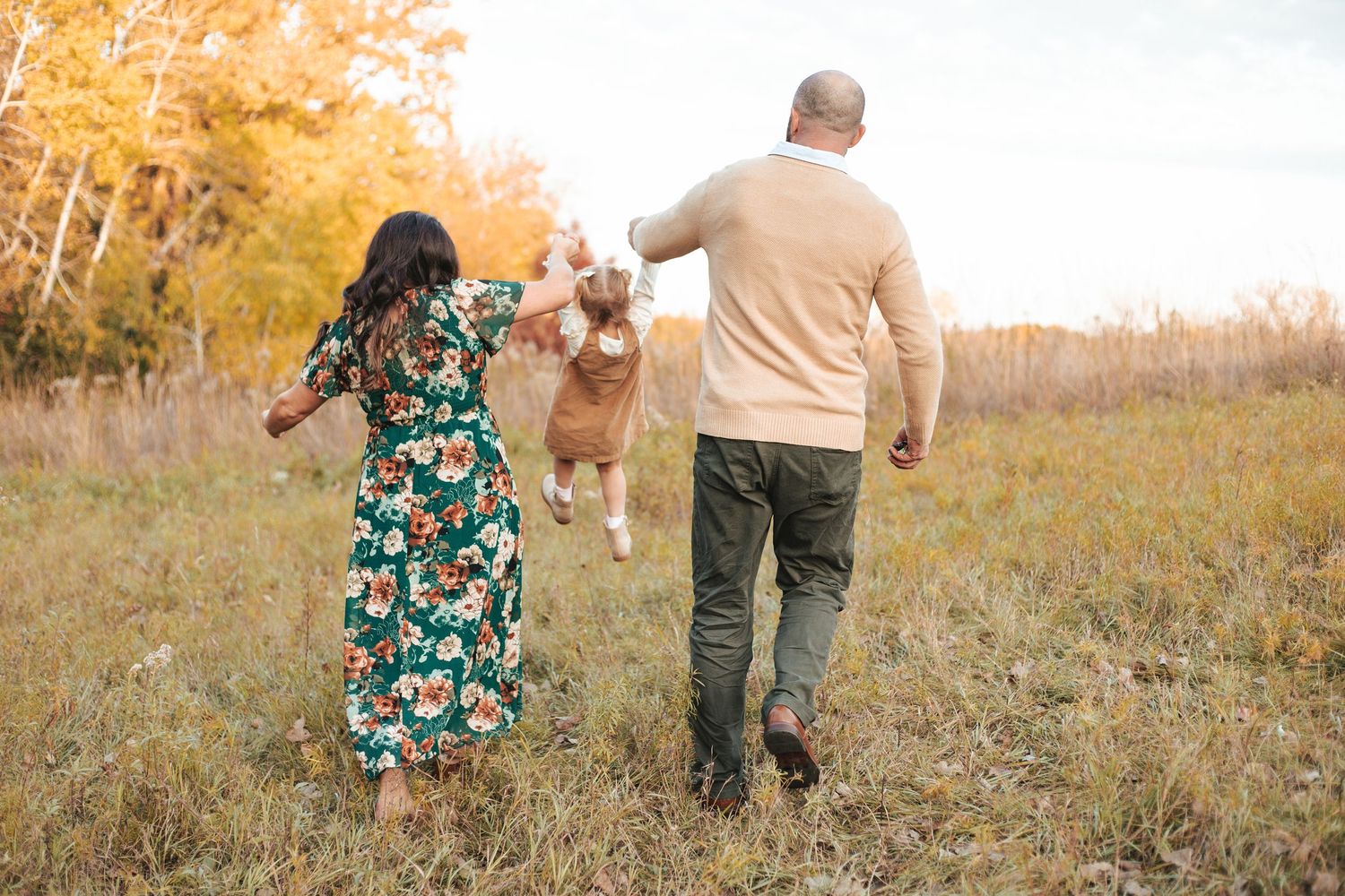 Family walking through autumn field in Lakeville, parents swinging young child between them for lifestyle family photo session