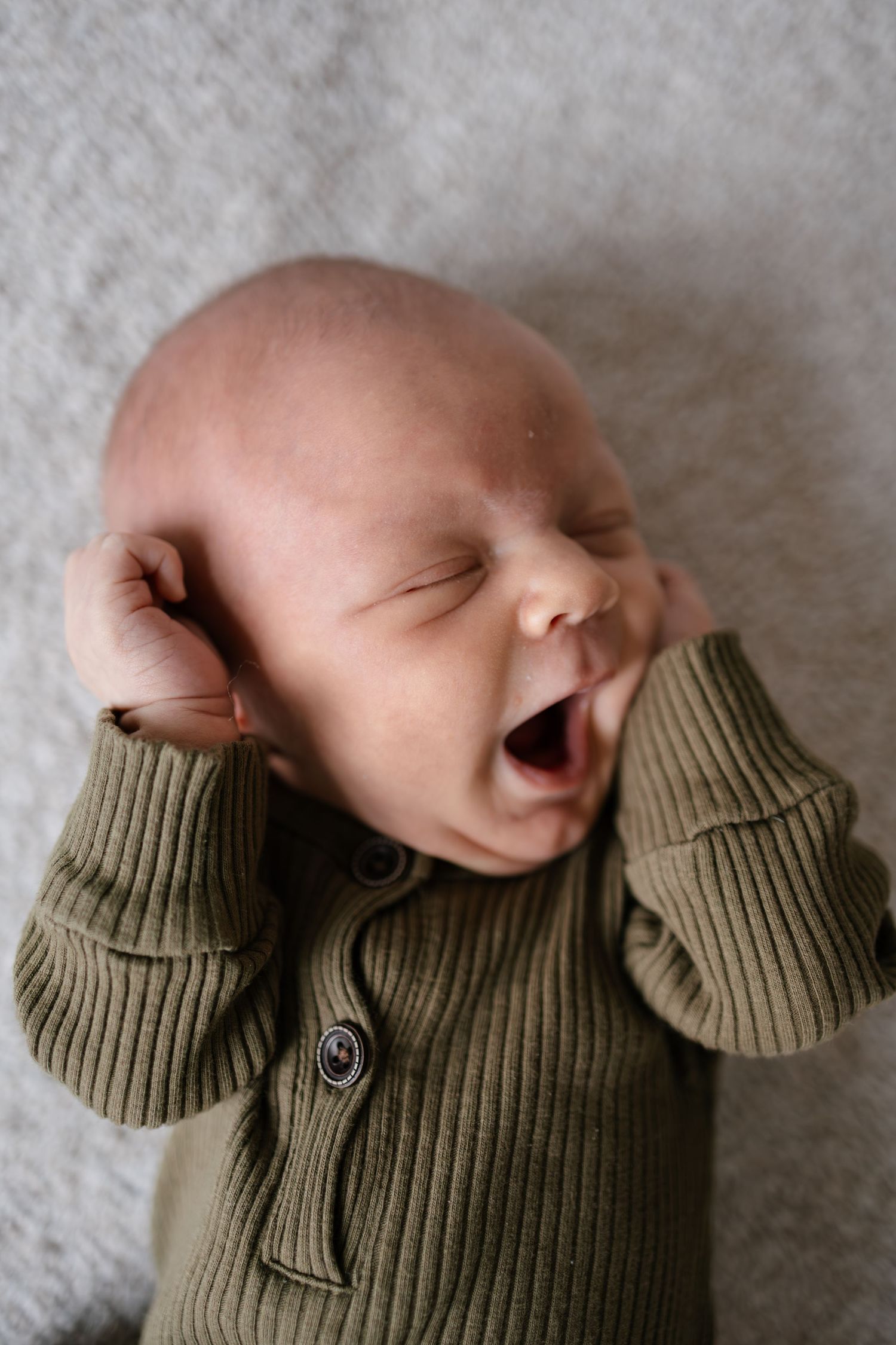 A sleeping baby wearing a knit olive sweater lies on a soft gray blanket, taken by western Wisconsin newborn photographer.