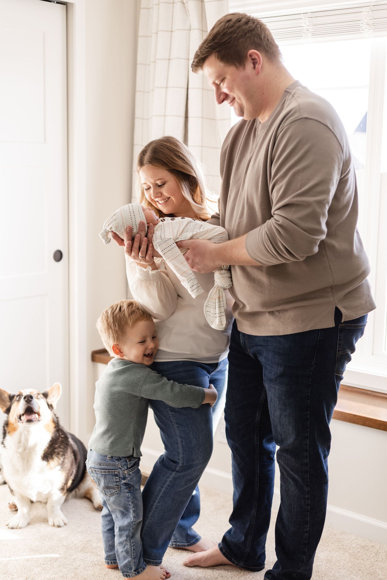 Parents cradle their newborn in a bright bedroom while a child hugs his mother during Lake Elmo in-home newborn session.
