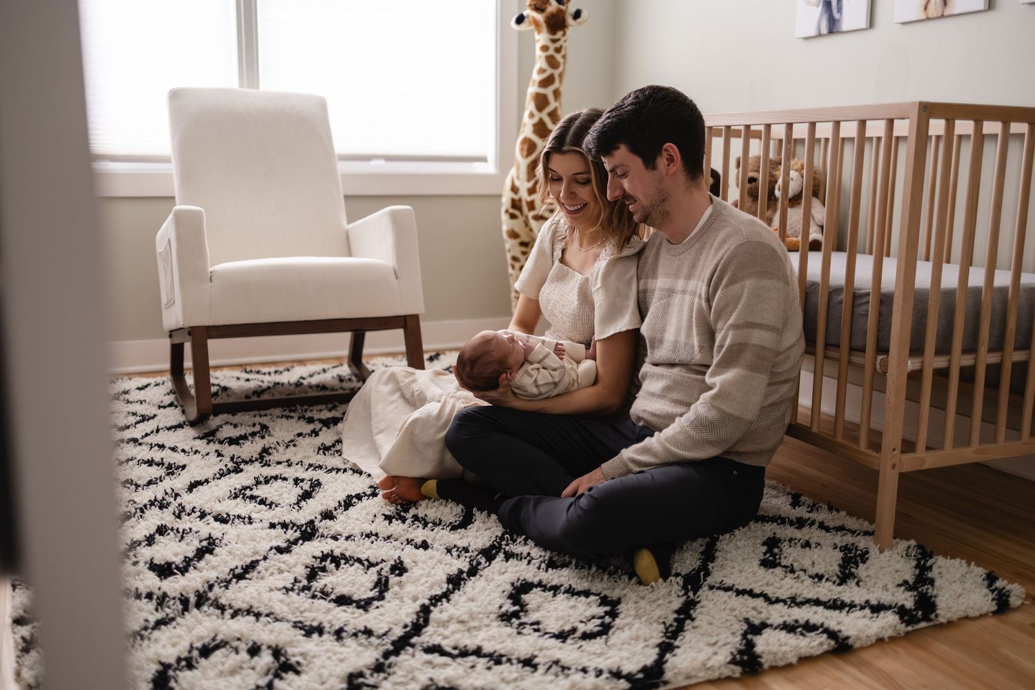 Parents sitting with their baby in cozy nursery room decorated with a geometric patterned rug during in-home newborn session in Twin Cities.
