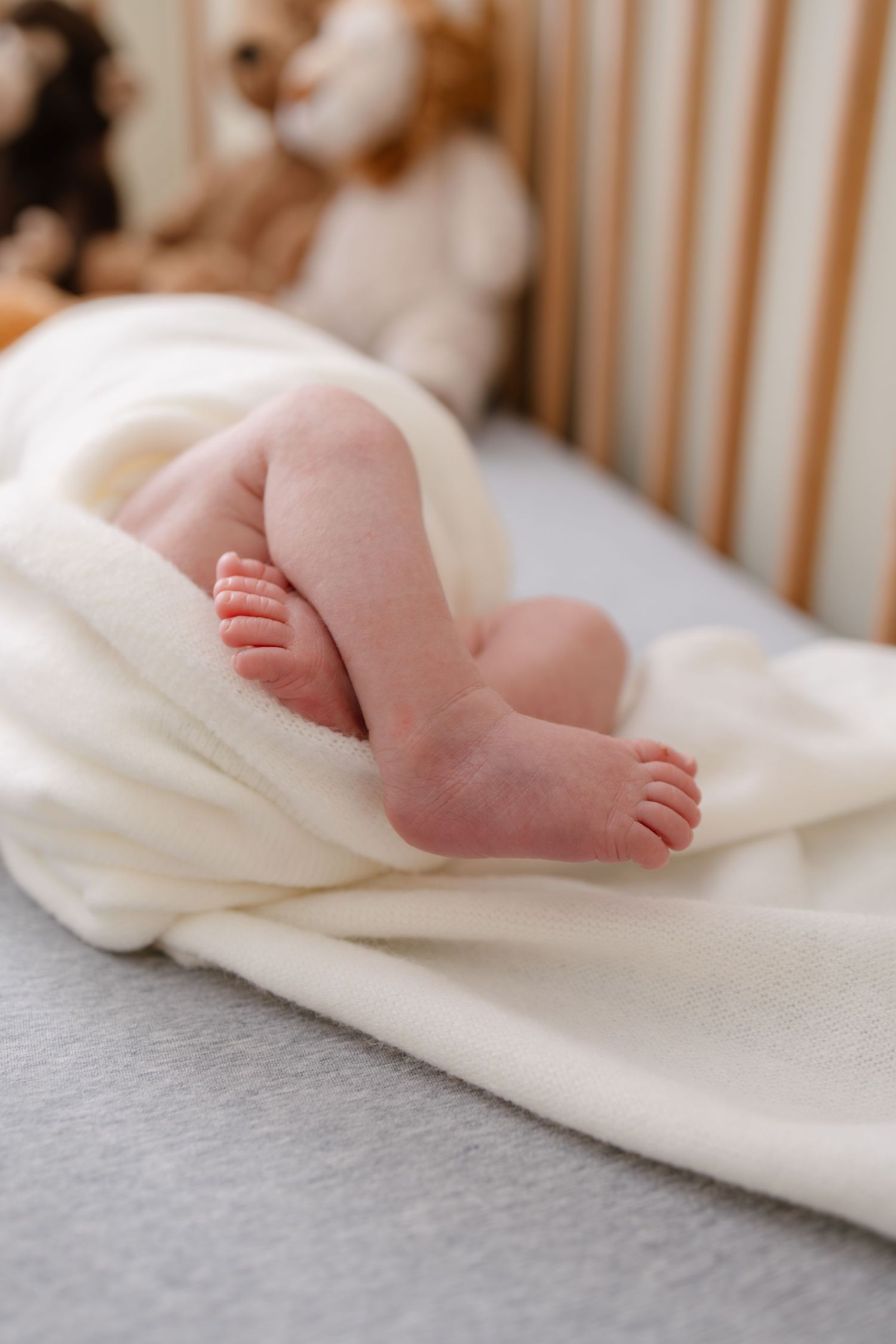 Close-up of tiny newborn baby feet peeking out from a soft white blanket in a wooden crib.