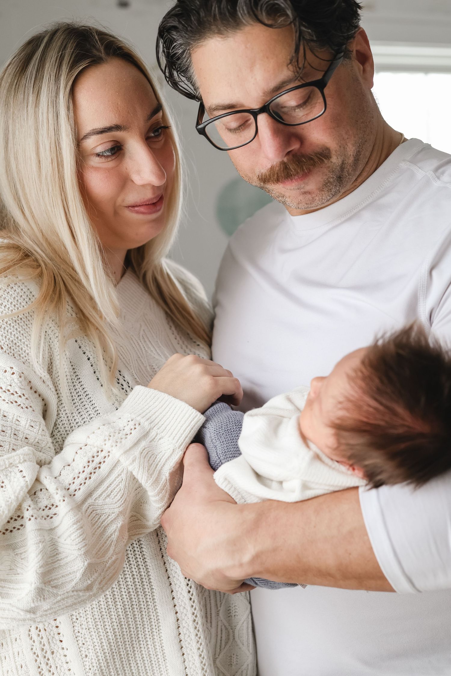 A couple in white clothing tenderly holds their newborn baby while sharing an intimate family moment at home in the Twin Cities.