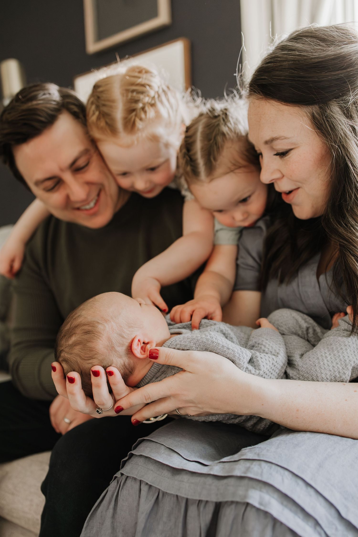 Happy family with parents and three young children lovingly gazing at their newborn baby during Twin Cities in-home newborn session.
