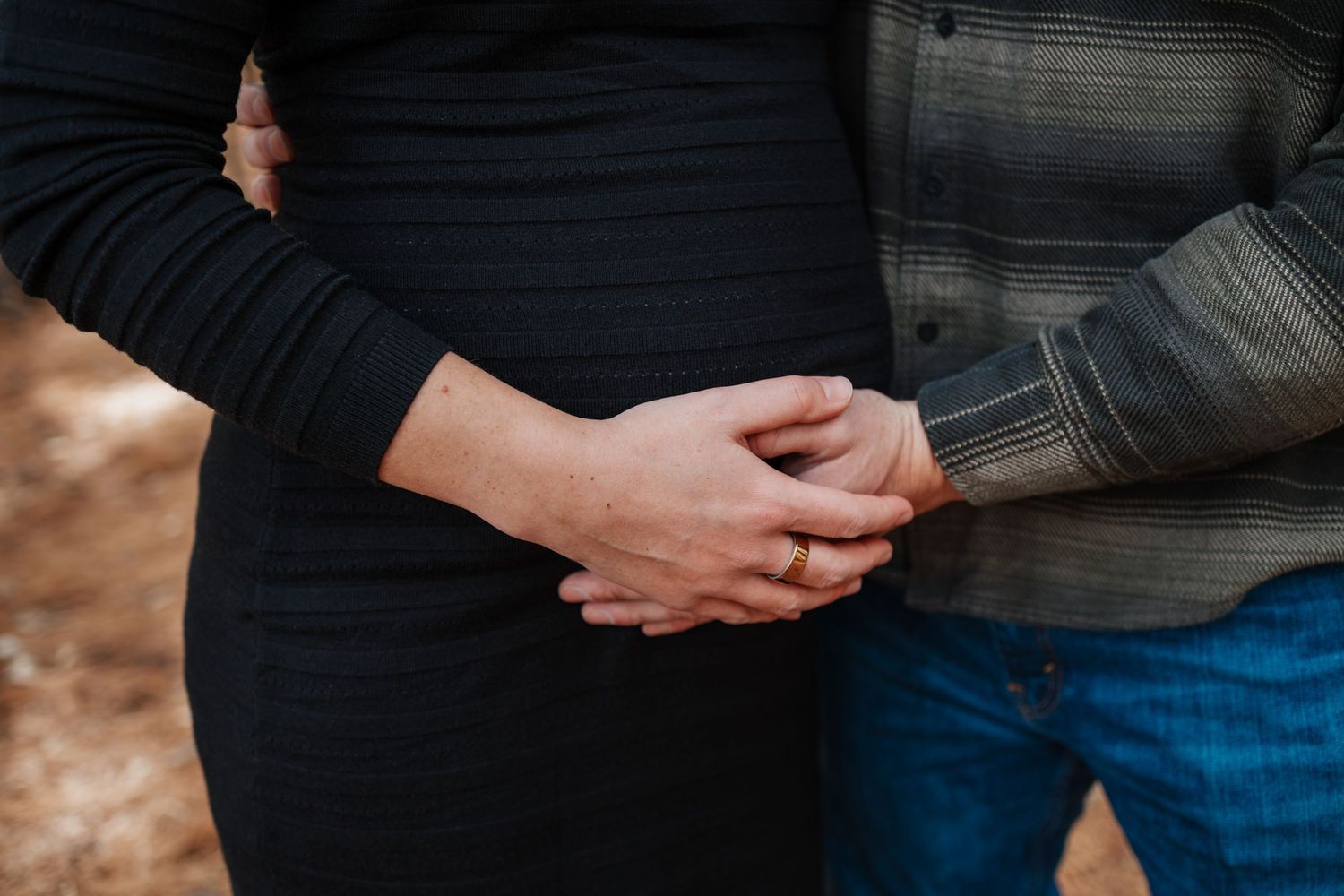 Close-up shot of two people cradling a pregnant belly while wearing denim and black clothing, taken by Woodbury maternity photographer.