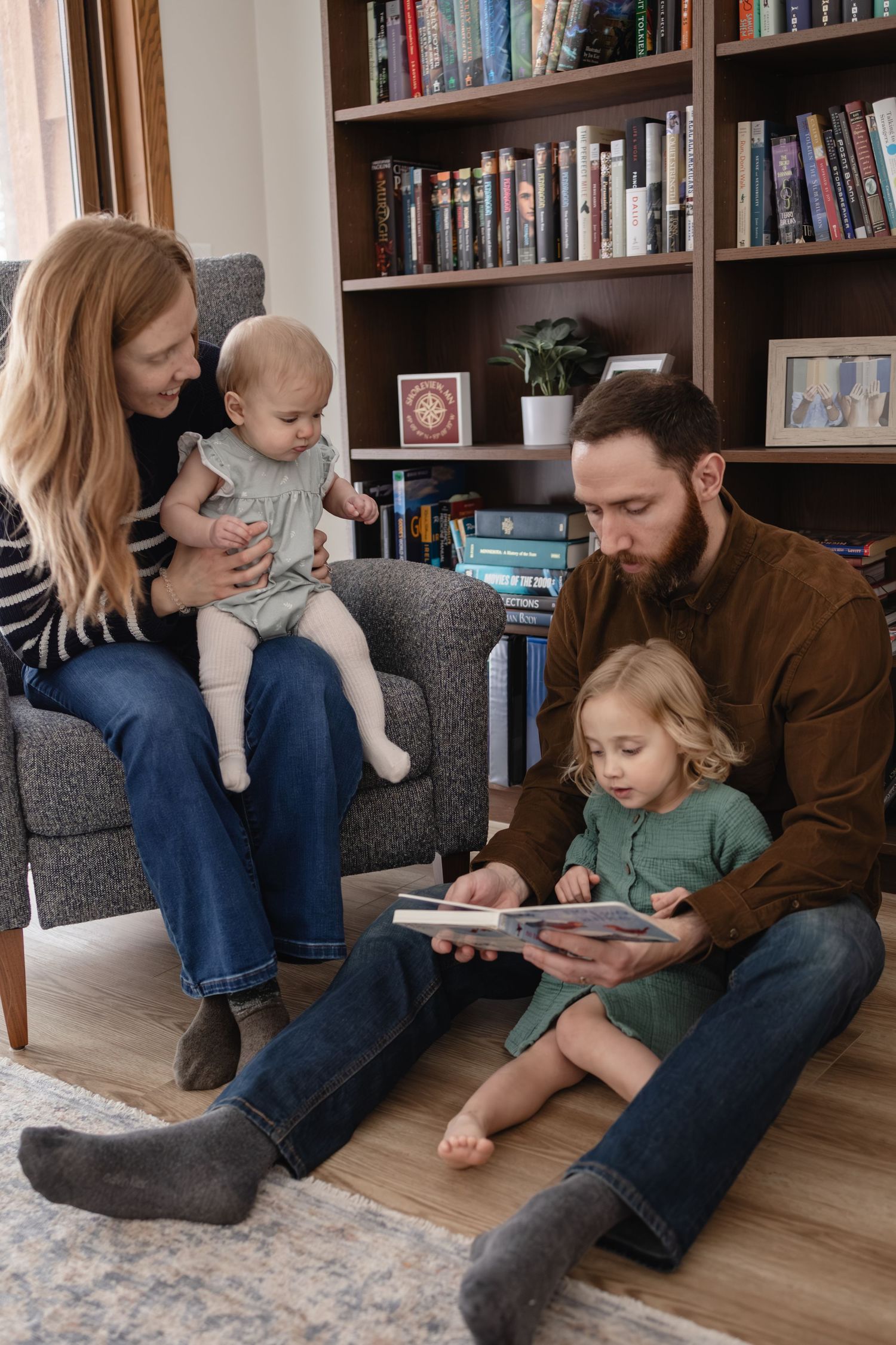 A family of four reads a book together in a cozy living room with bookshelves in the background in Shoreview, MN.