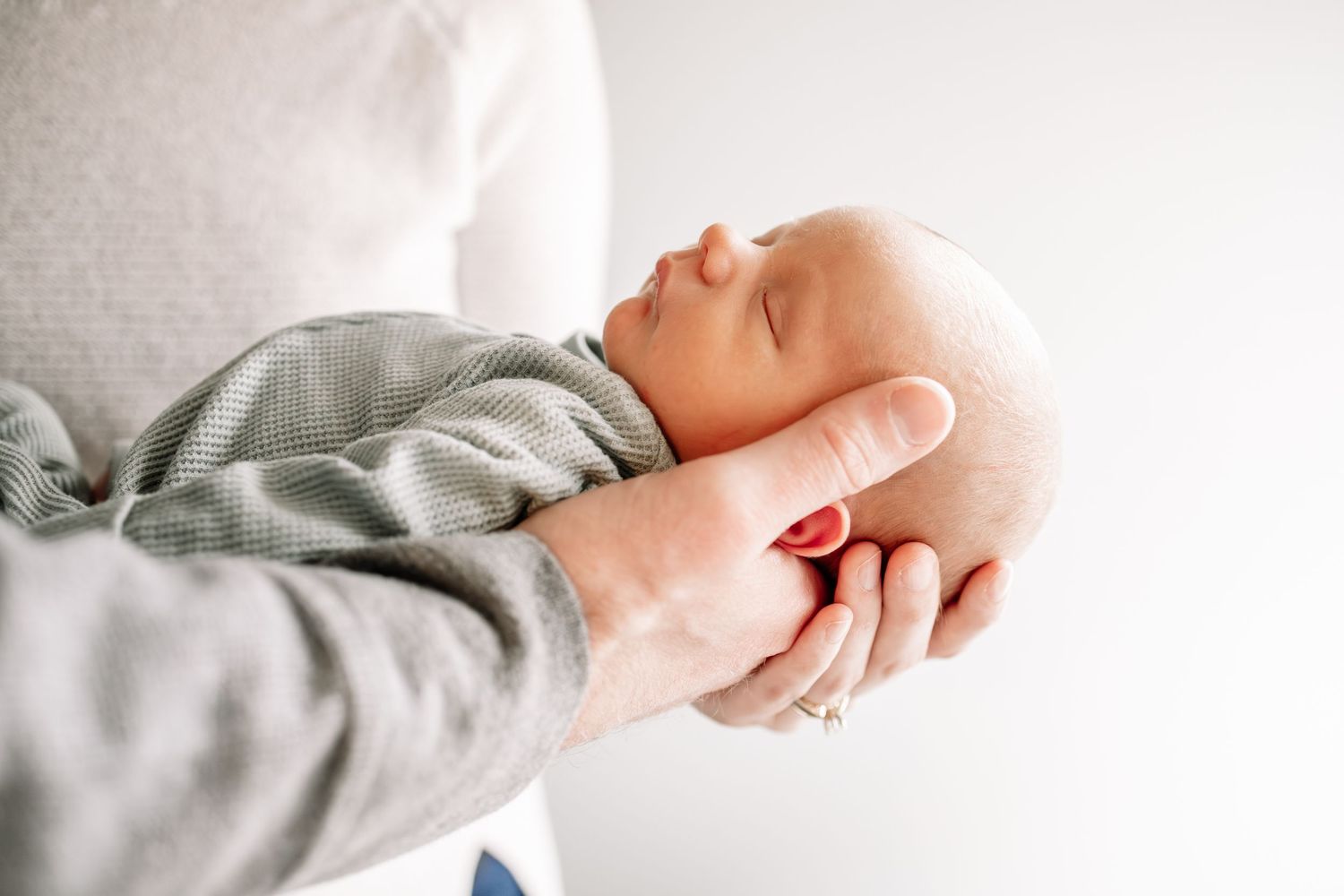 A mother gently cradles a sleeping newborn baby in her hands against a soft white background taken by Woodbury newborn photographer.