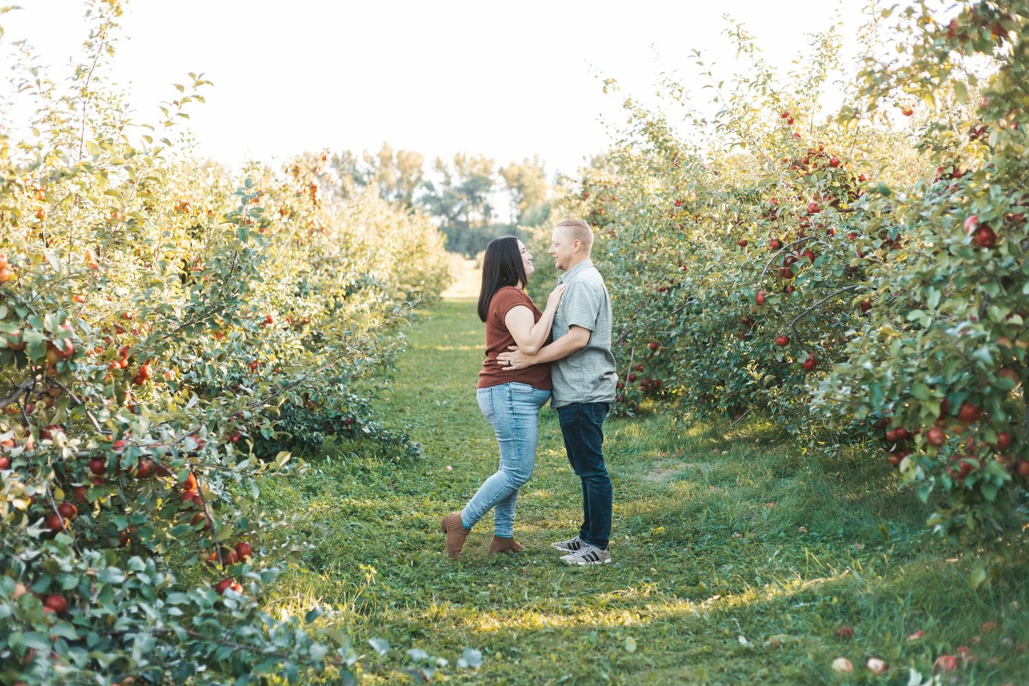 Two people walk together through a scenic apple orchard on a bright autumn day during Lakeville orchard mini session.
