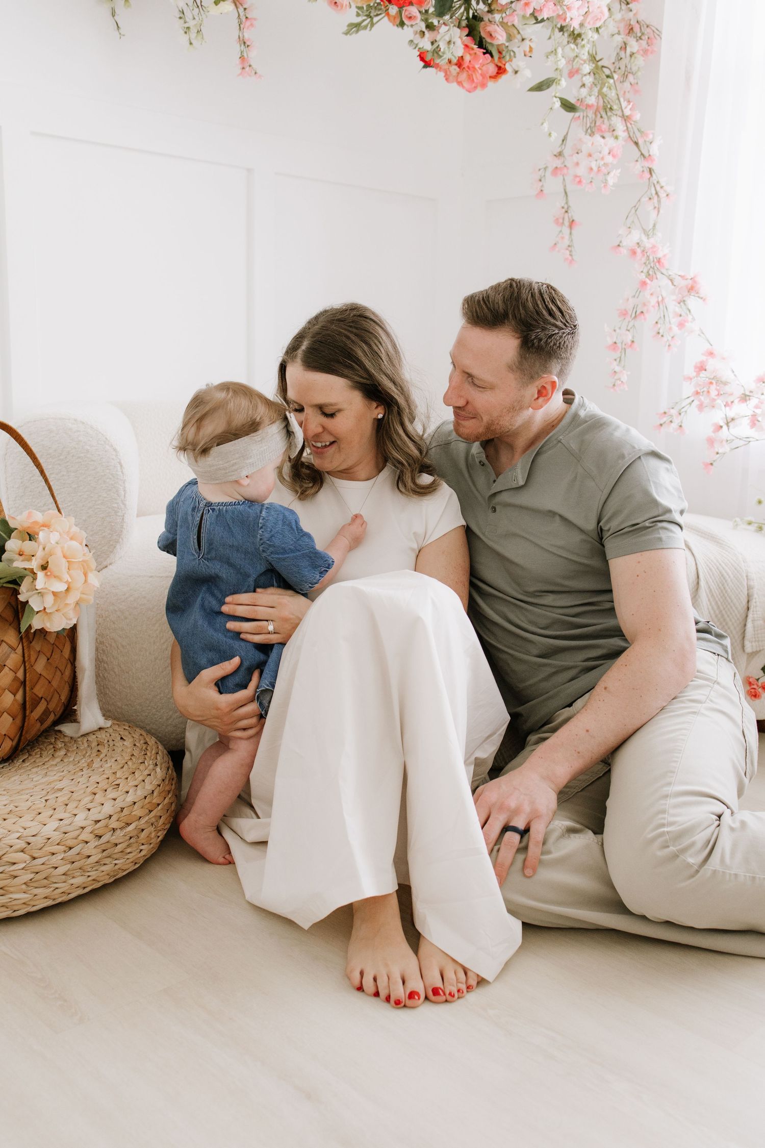 A happy family with a baby girl sits together in a bright, floral-decorated studio for a professional photo session in Lakeville.