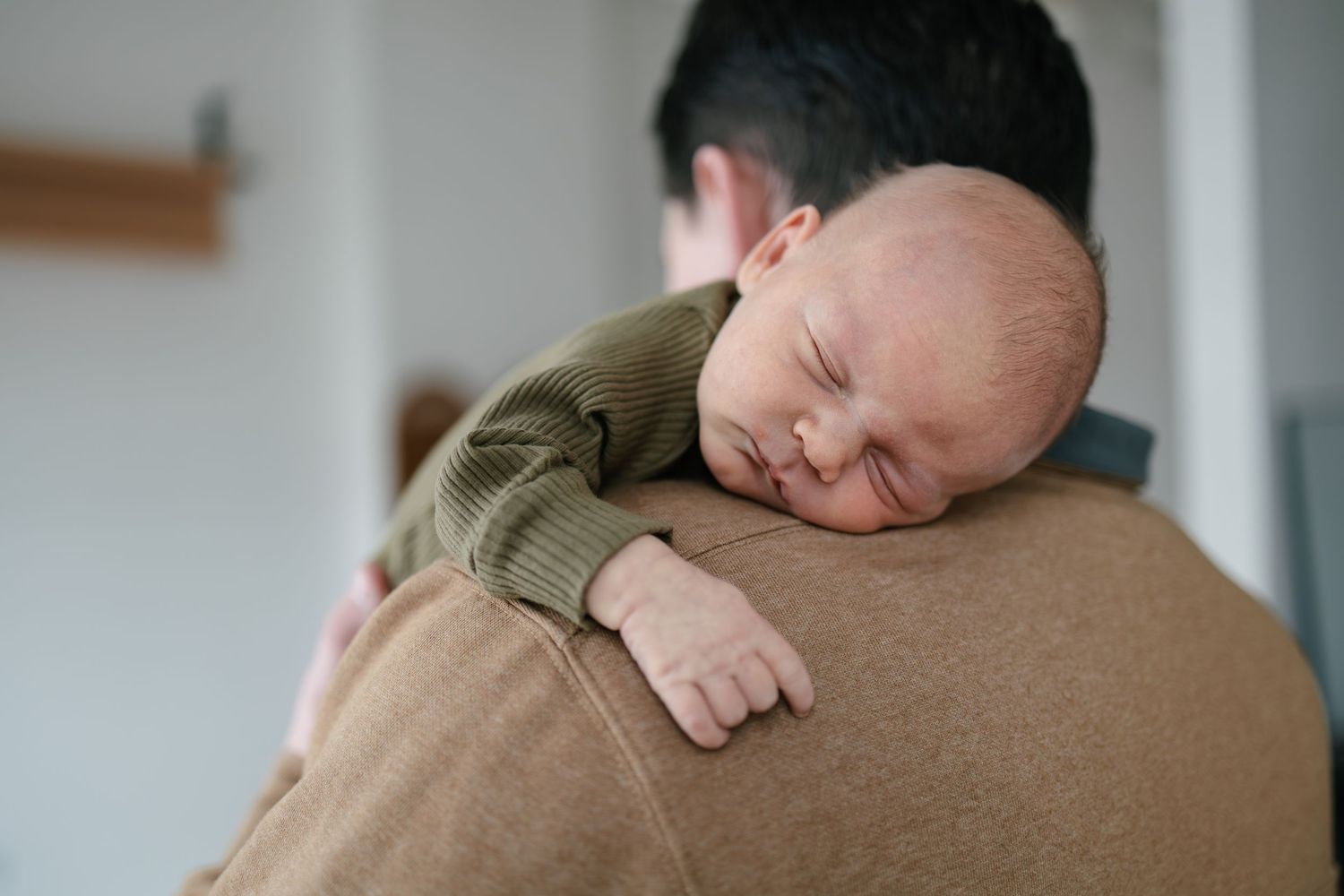 A sleeping newborn baby rests peacefully on a father's shoulder, taken by Woodbury newborn photographer.