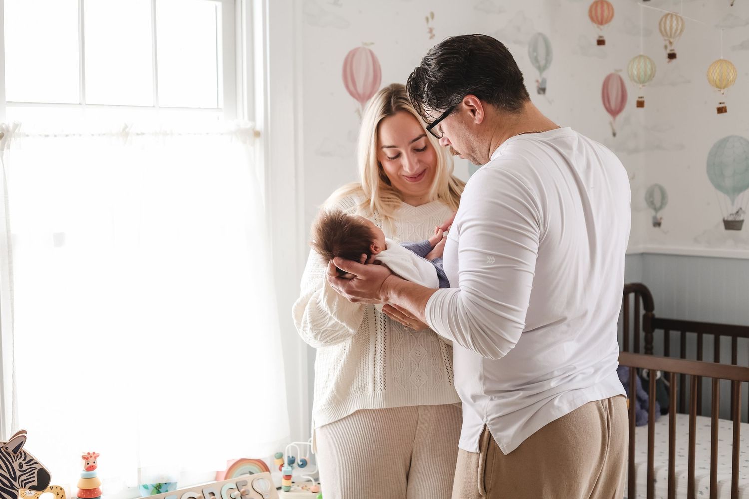 A couple shares tender moments in a nursery decorated with pastel balloons and wall decals, taken by Twin Cities newborn photographer.