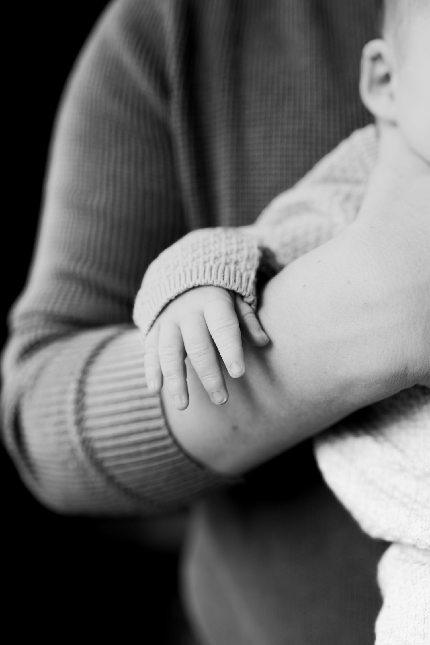 Photo of a parent cradling a baby, with the infant's tiny hand resting on the parent's arm during Twin Cities in-home newborn session.