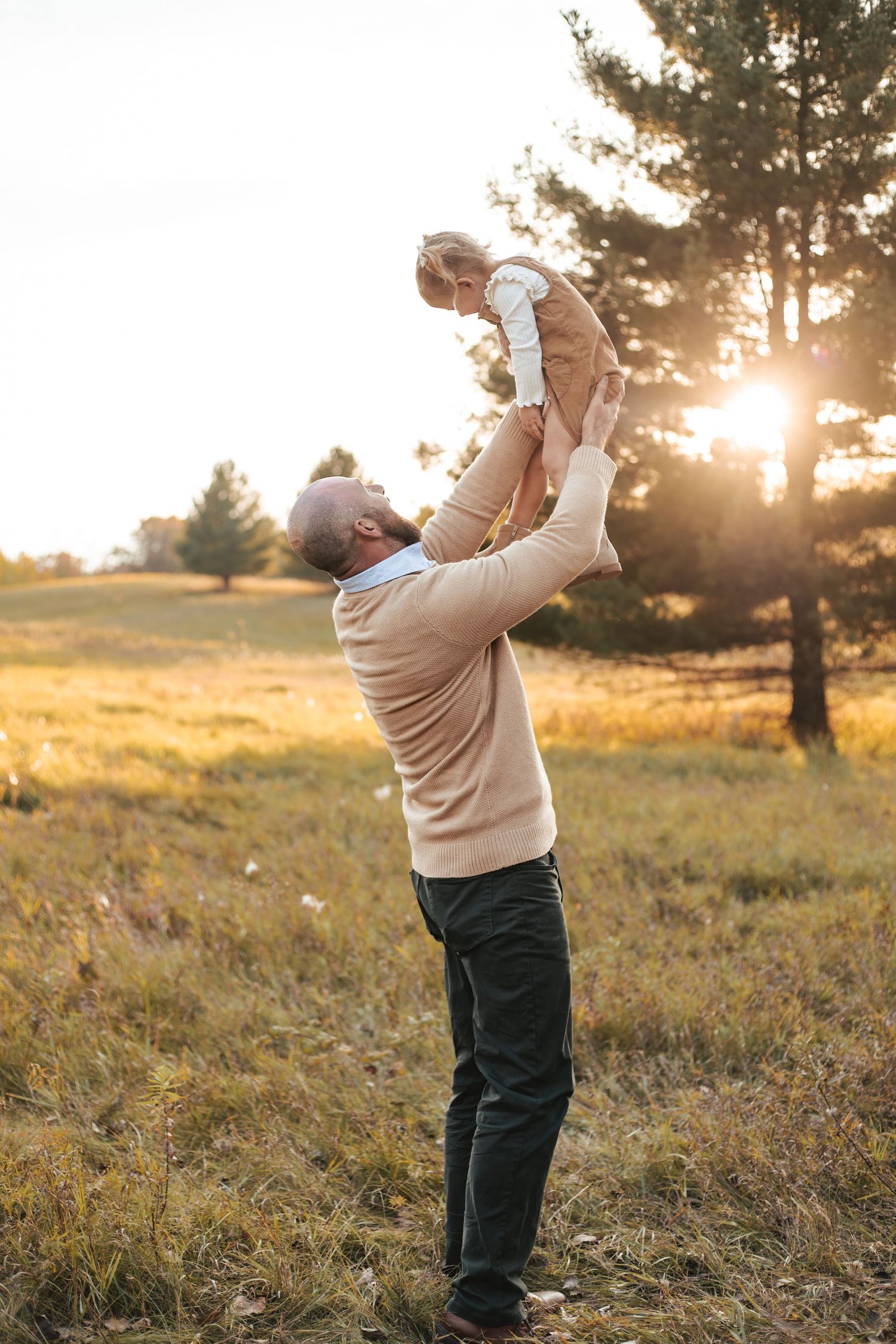Father lifting baby in the air at sunset in a golden Lakeville field, sharing a joyful outdoor moment together during fall mini session