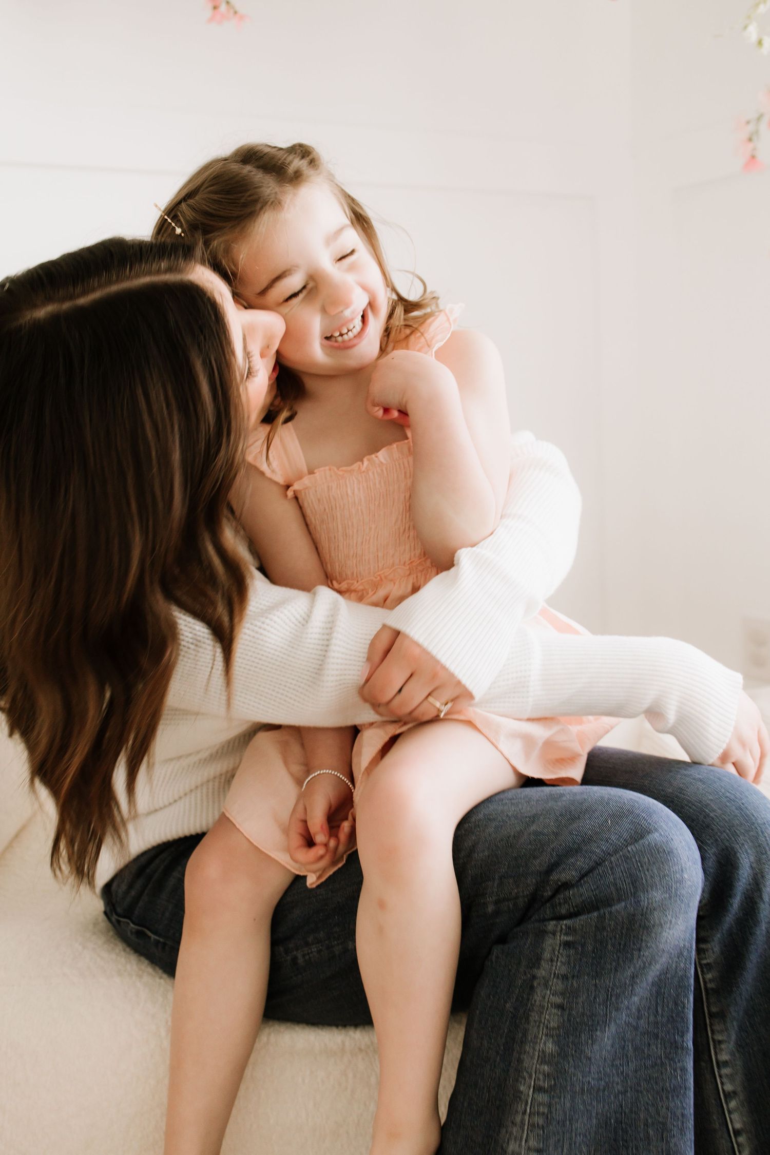 A mother and daughter share a joyful embrace, both smiling, dressed in white and pink outfits during motherhood mini session in Lakeville
