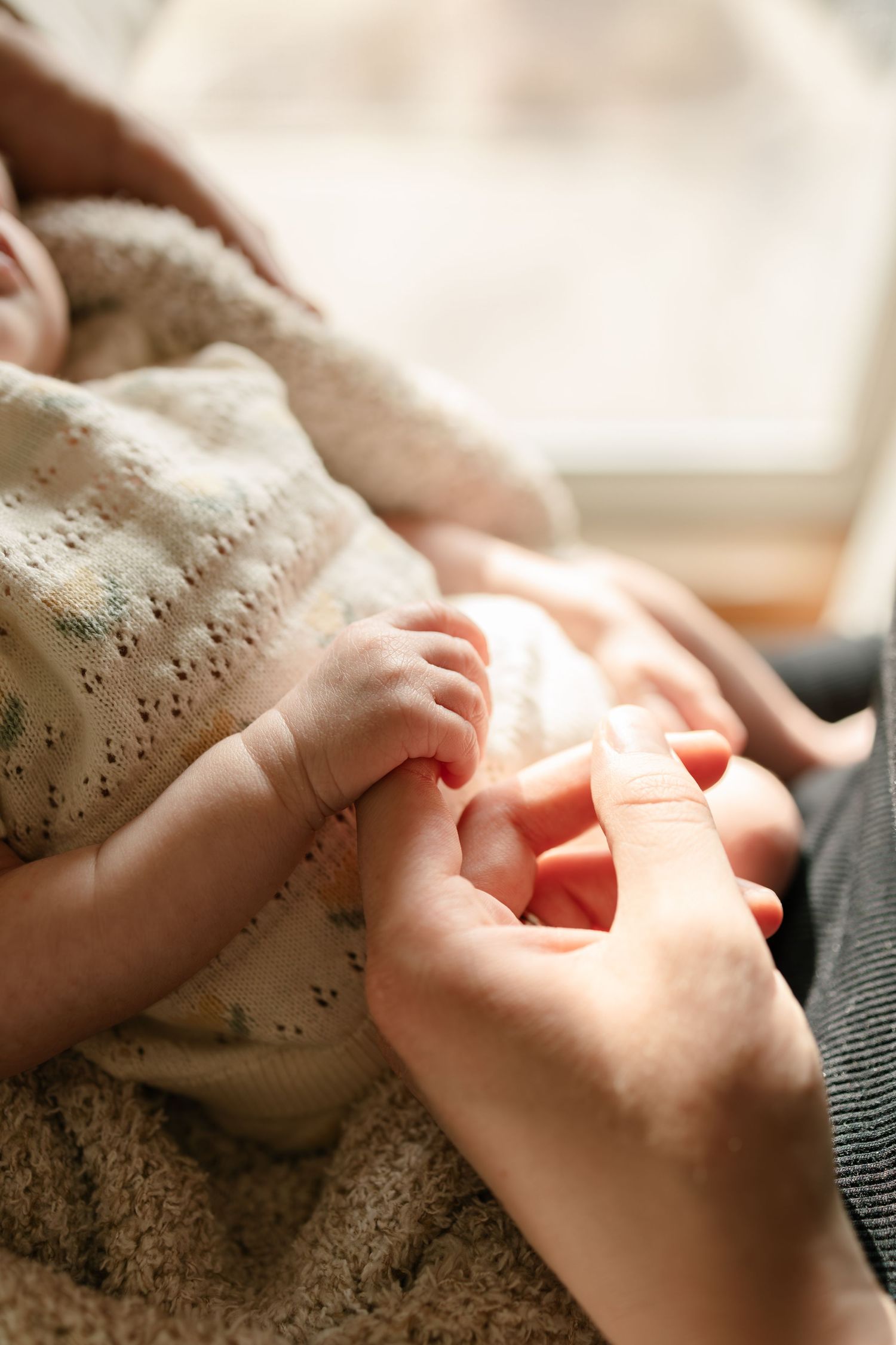 A newborn baby gently grips an adult finger while wrapped in a soft knit blanket captured by Twin Cities newborn photographer.